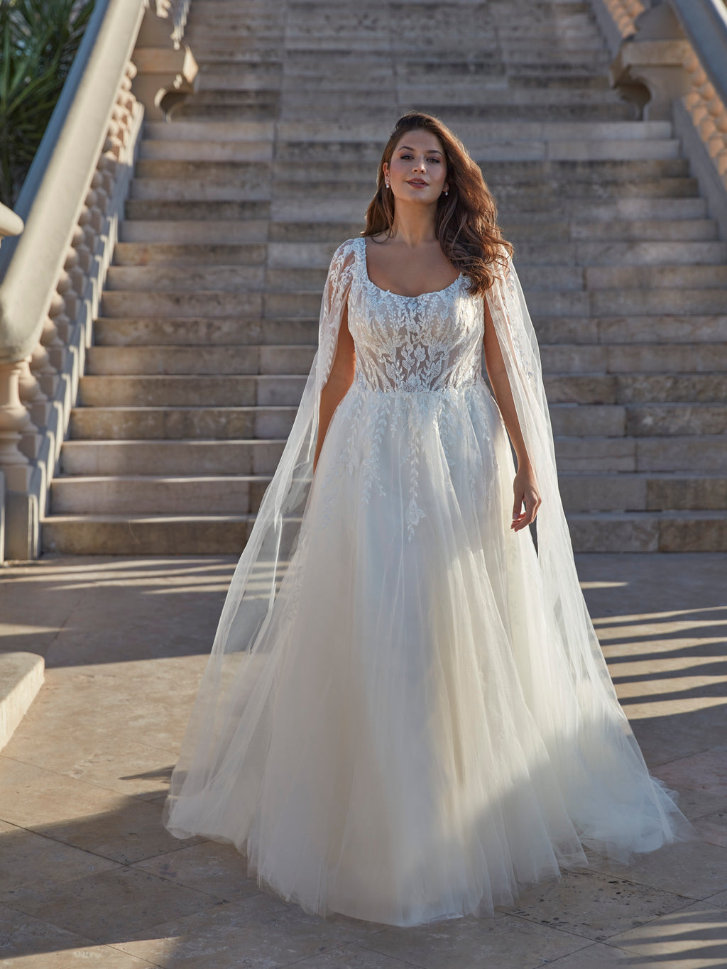 Woman in a white wedding dress with a cape standing on stone steps.