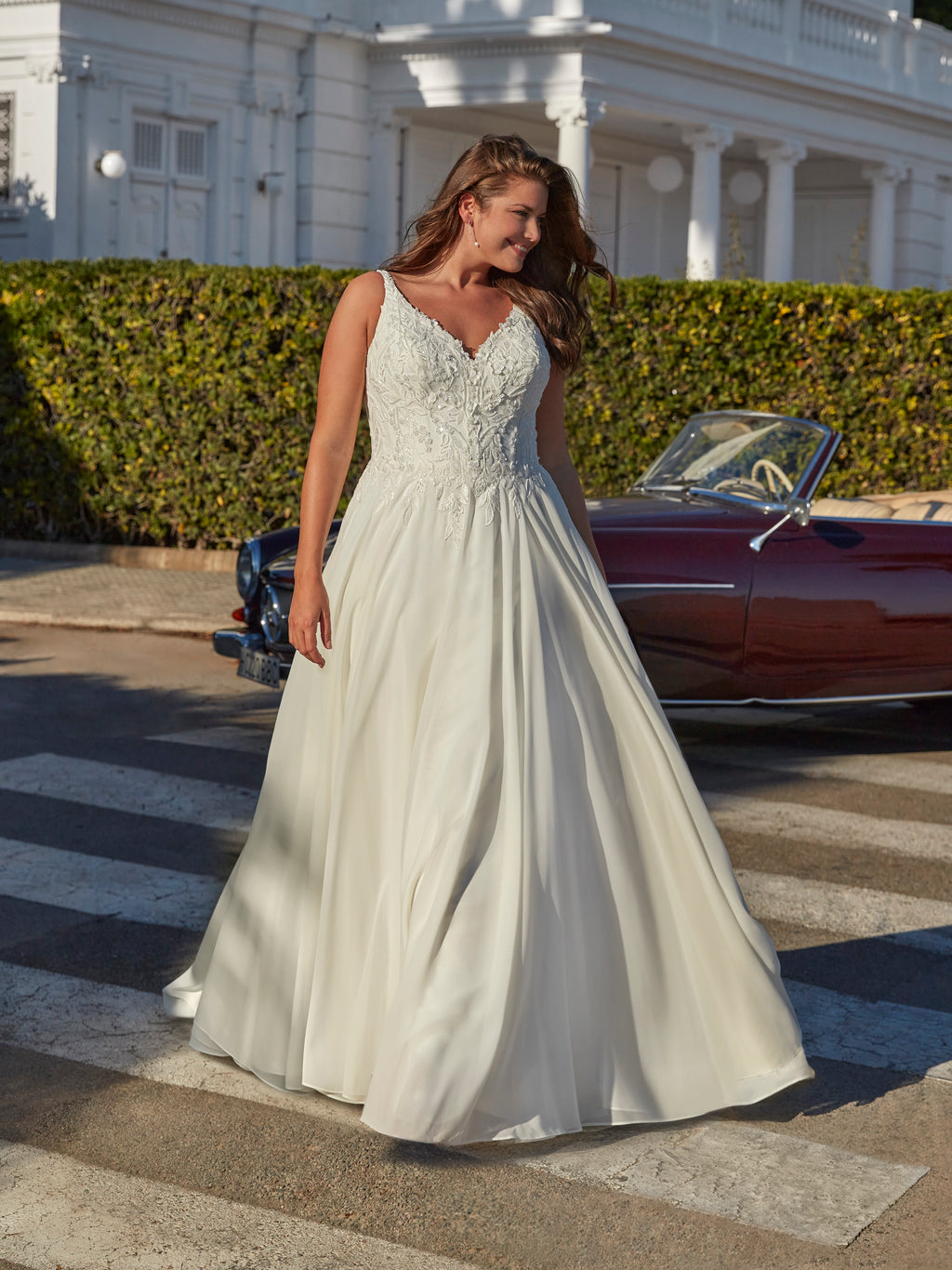 Woman in a white wedding dress standing on a street with a vintage car in the background.