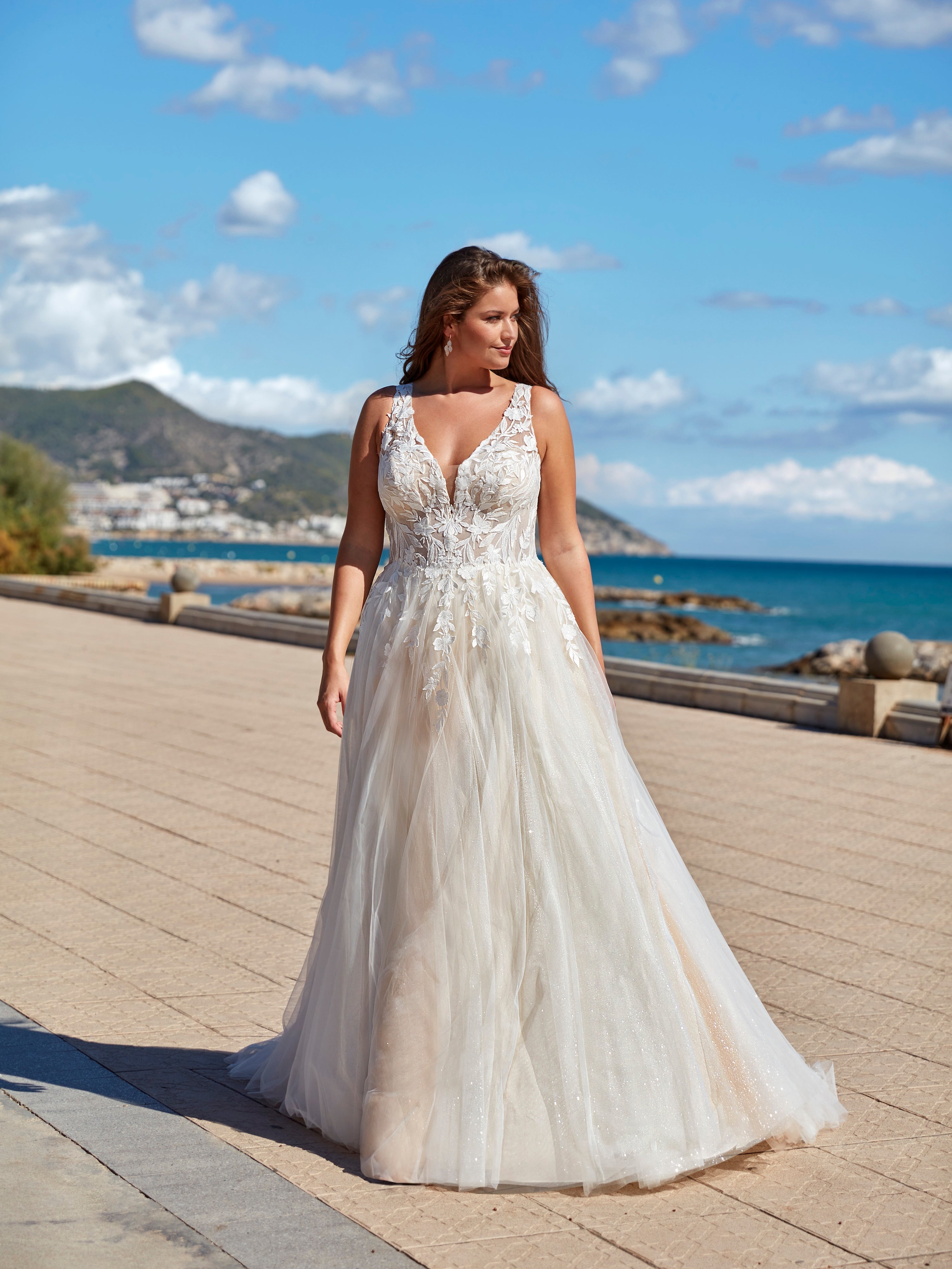 Woman in a white wedding dress standing on a wooden boardwalk by the ocean.