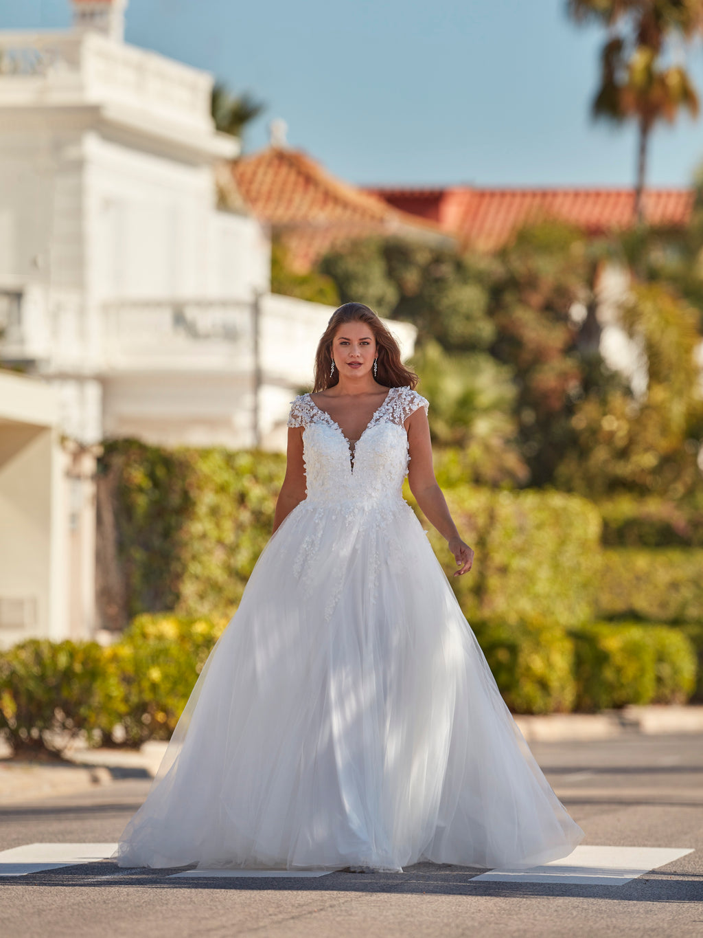 Woman in a white wedding dress standing on a street with greenery and buildings in the background