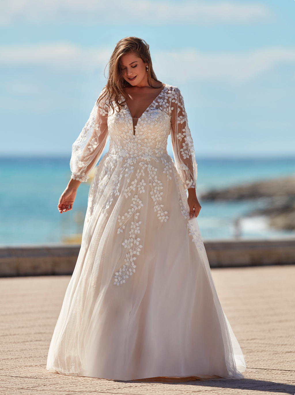 Woman in a white wedding dress with floral details by the ocean.