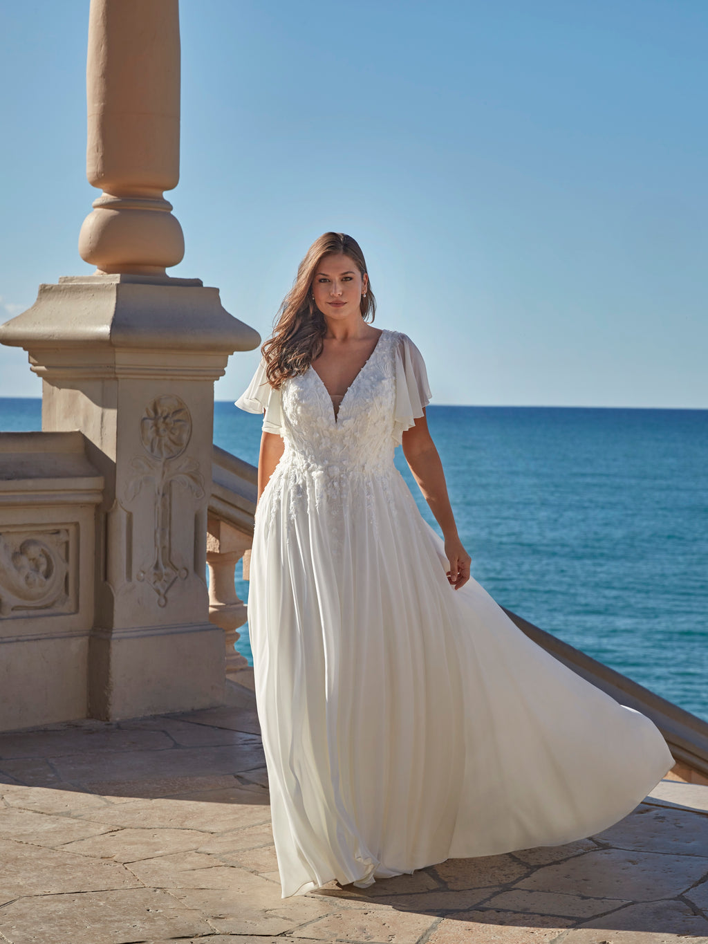 Woman in a white dress standing by the ocean.