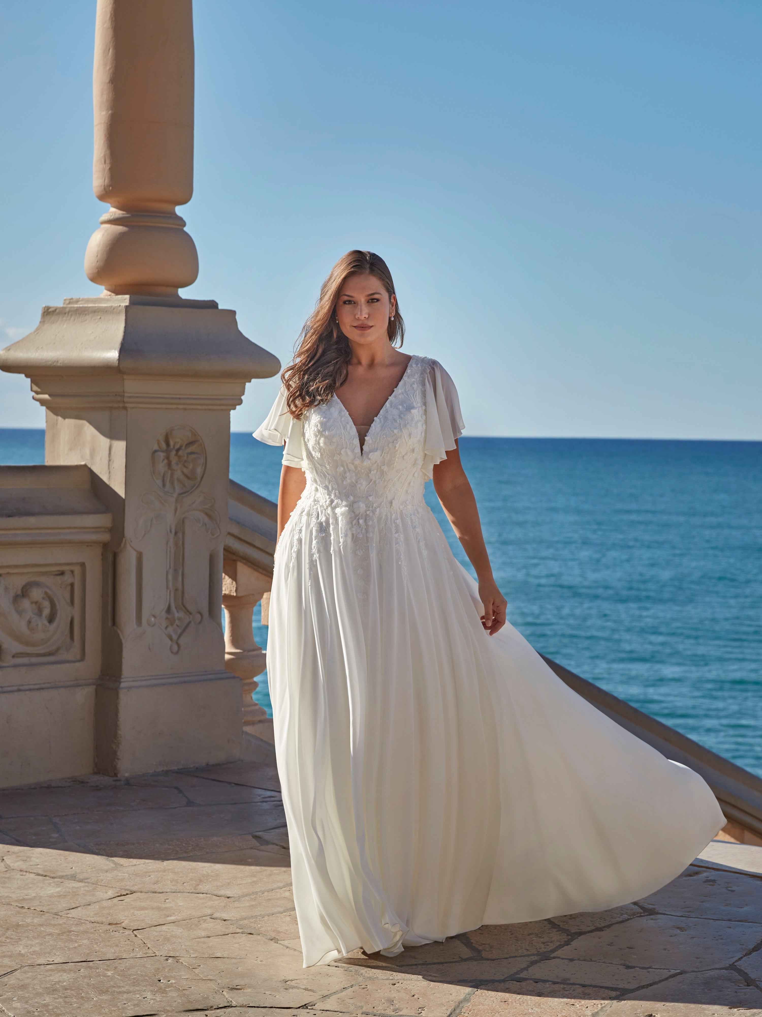 Woman in a white dress standing by the ocean.