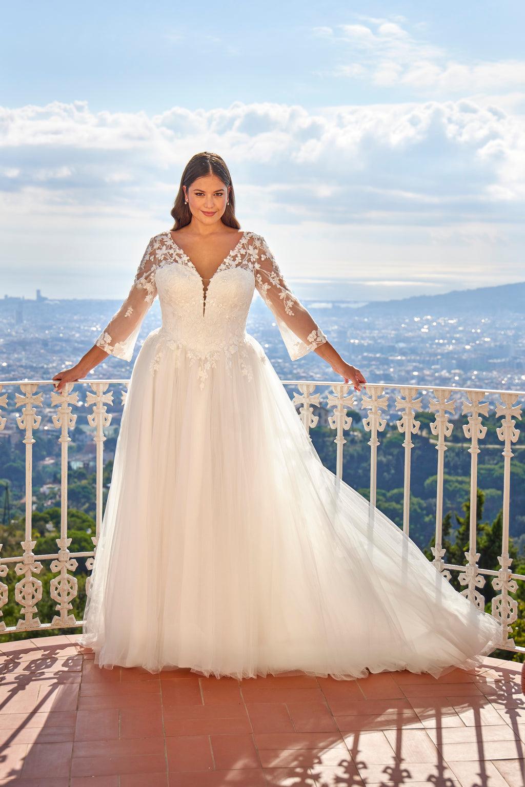 Woman in a white wedding dress standing on a balcony with a scenic view.