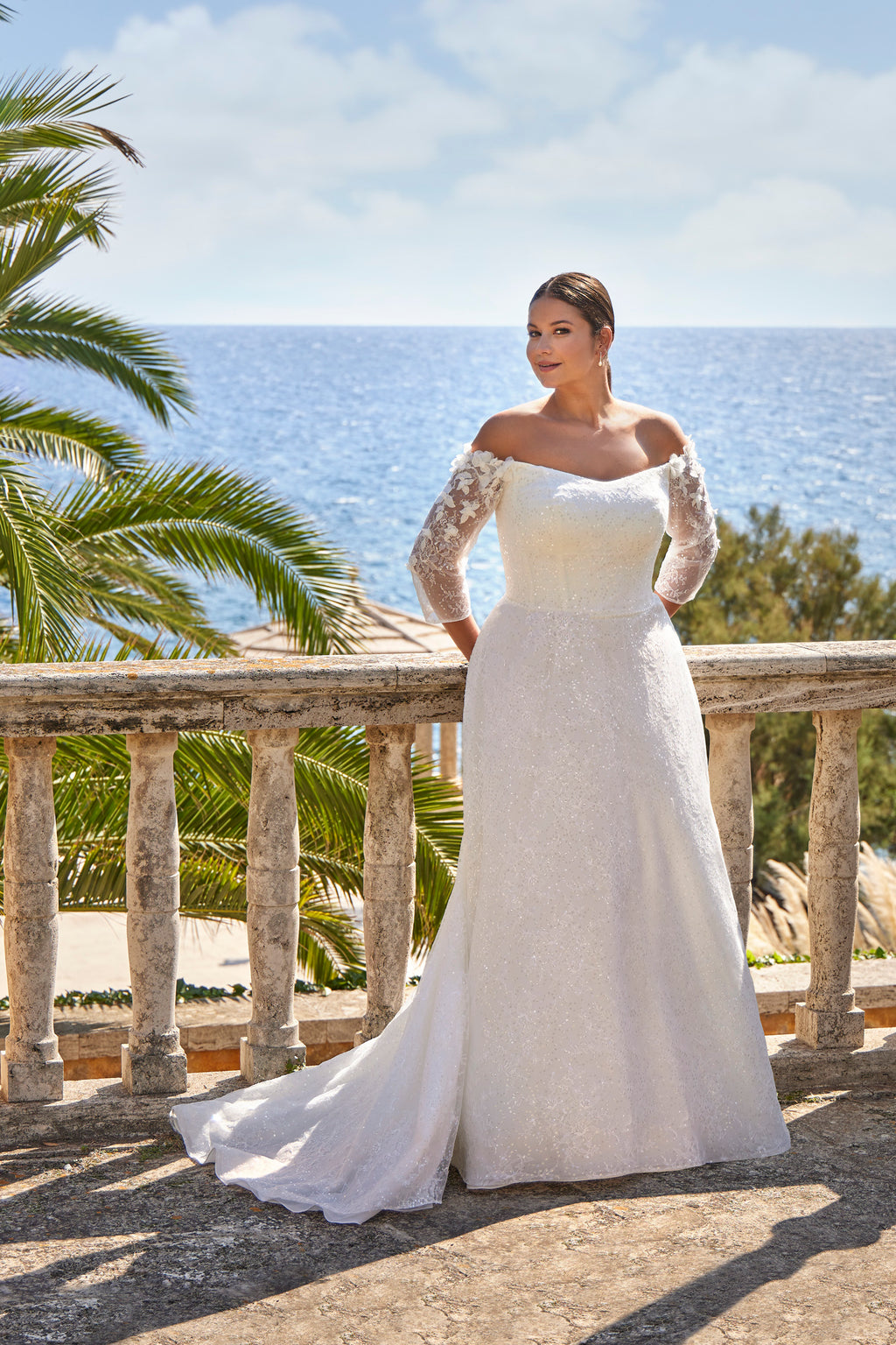 Woman in a white wedding dress with lace sleeves standing on a balcony with ocean view
