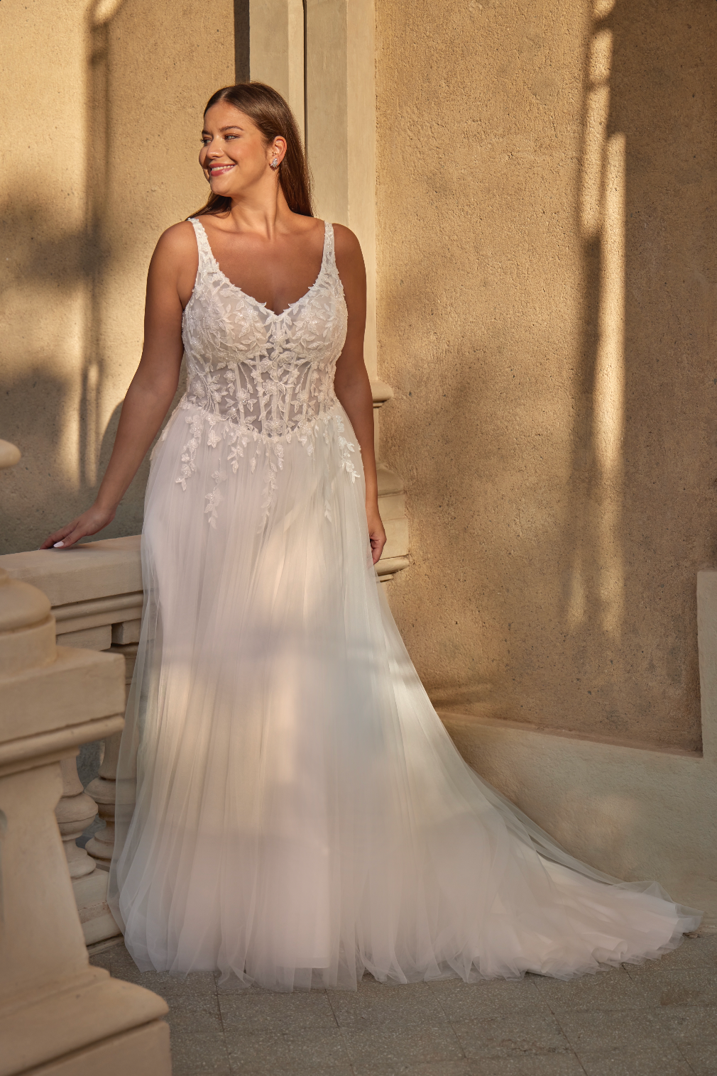 Woman in a white wedding dress standing outdoors with sunlight casting shadows.