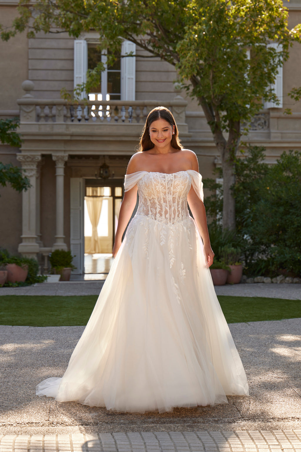 Woman in a white off-shoulder wedding dress standing in front of a classical building.
