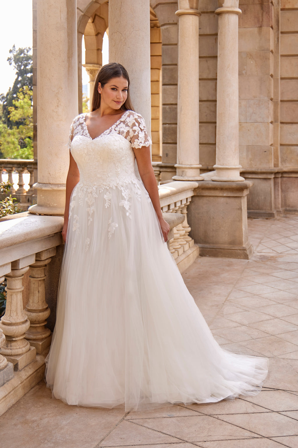 Woman in a white wedding dress standing on a stone balcony with columns.