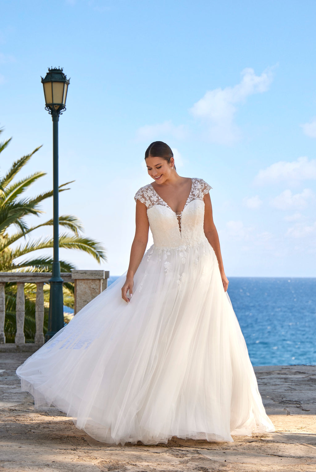 Woman in a white wedding dress standing by the sea with palm trees in the background