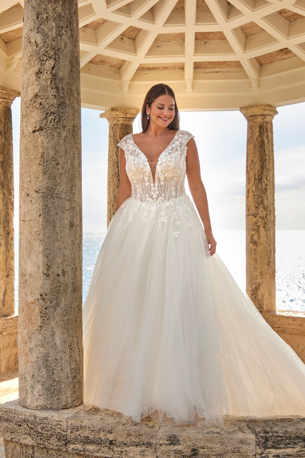 Woman in a white wedding dress standing under a stone archway with columns.