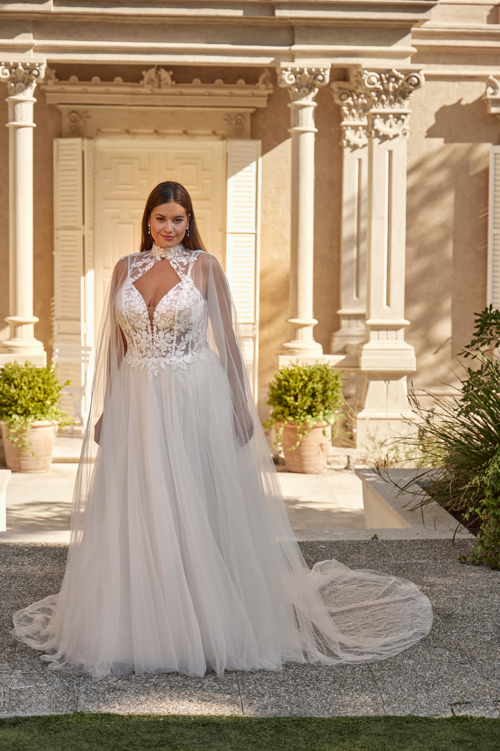 Woman in a white wedding dress with a long train standing in front of a classical building.