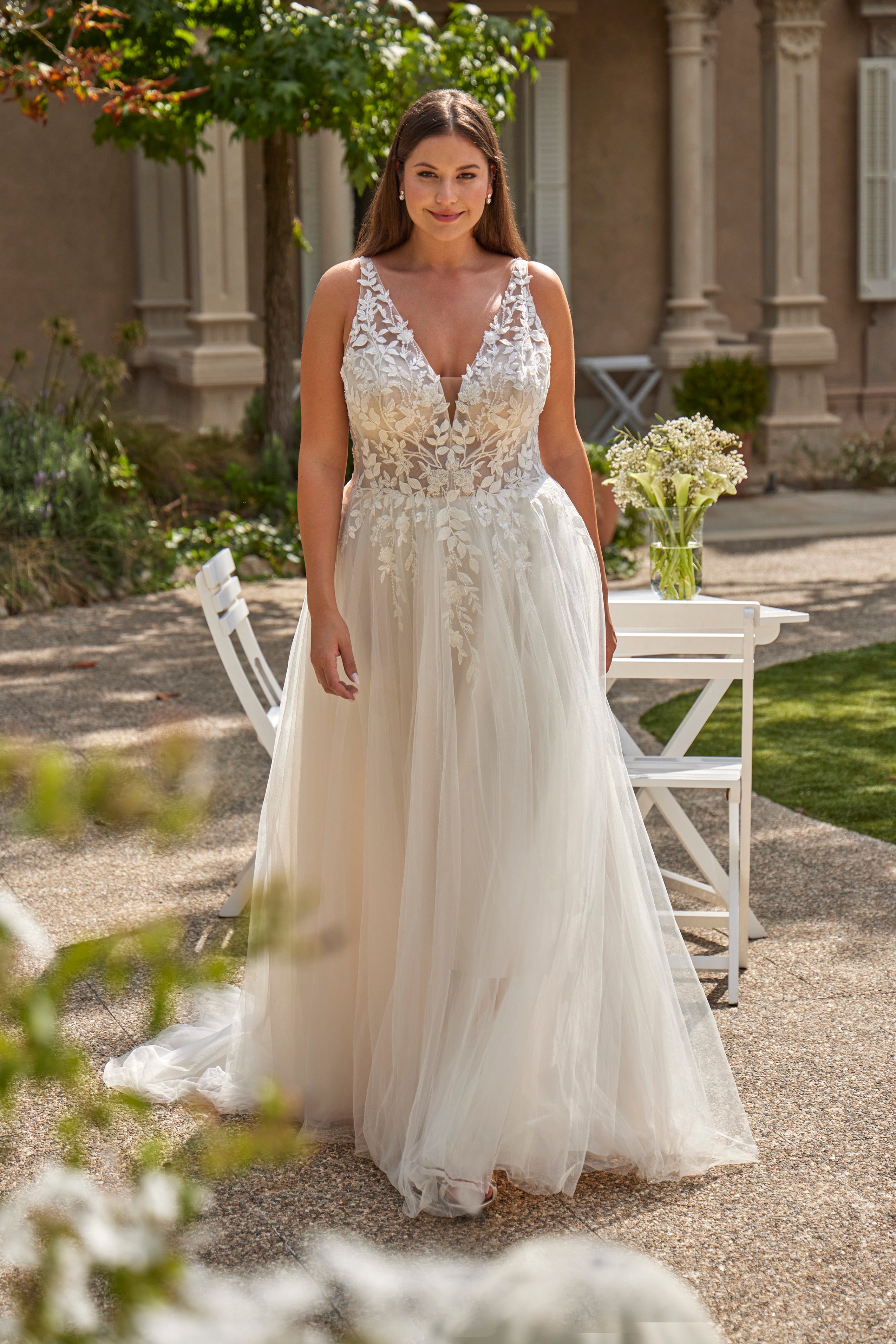 Woman in a white wedding dress standing outdoors with floral decorations.