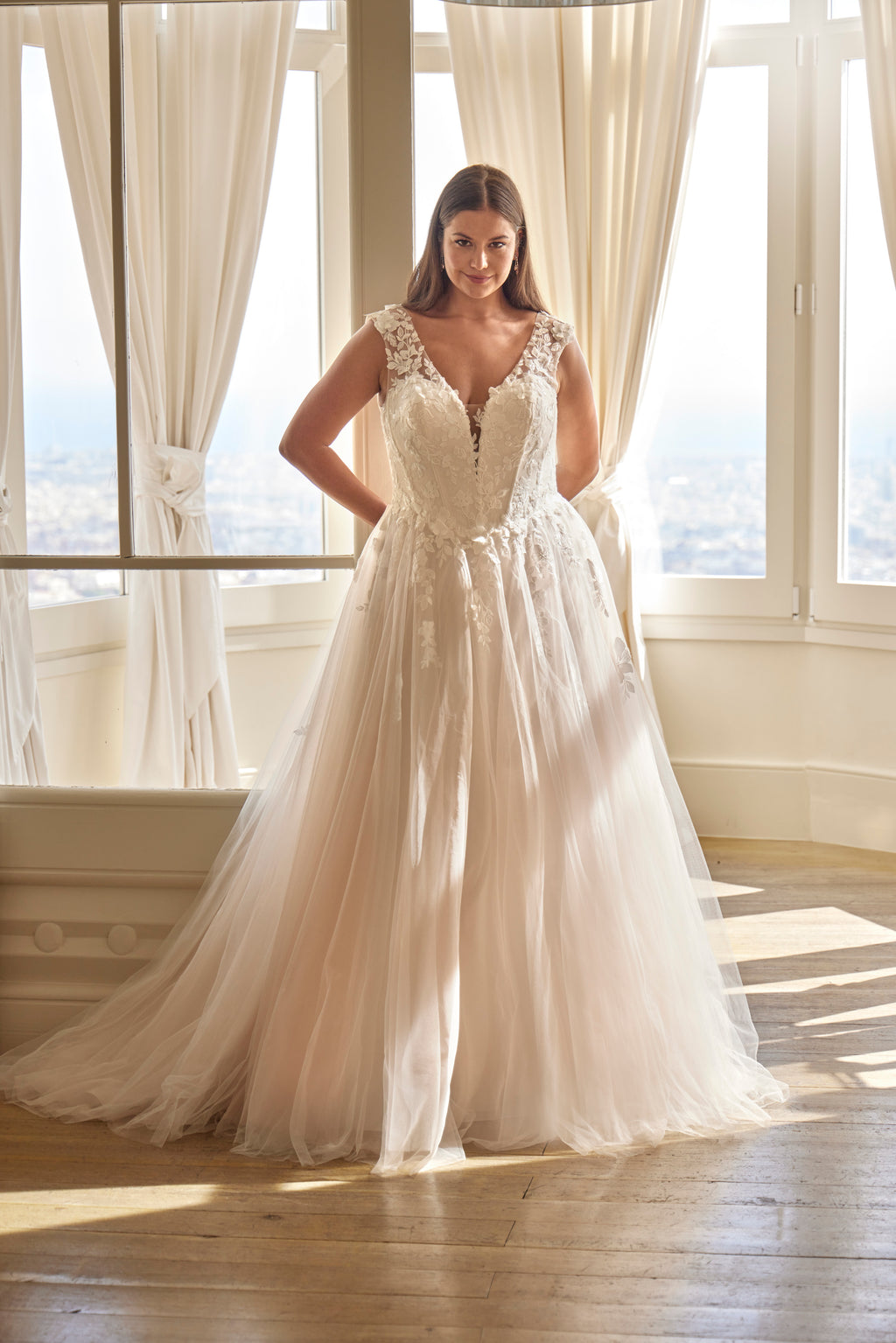 Woman wearing a white wedding dress in a bright room with large windows.
