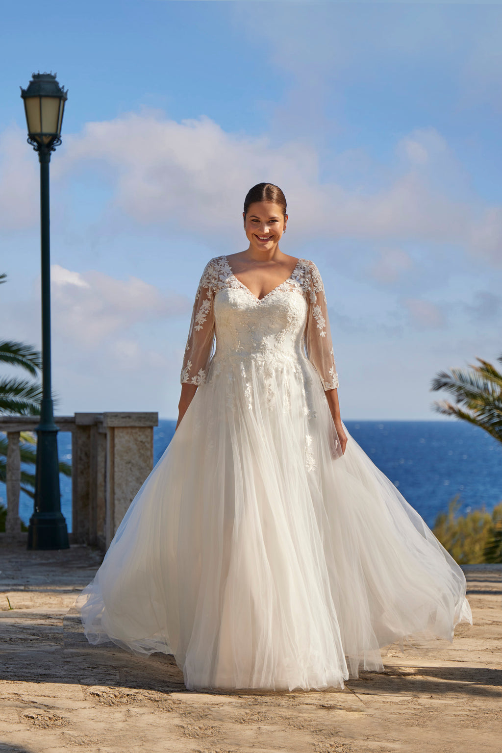 Woman in a white wedding dress standing on a wooden platform with ocean and sky in the background