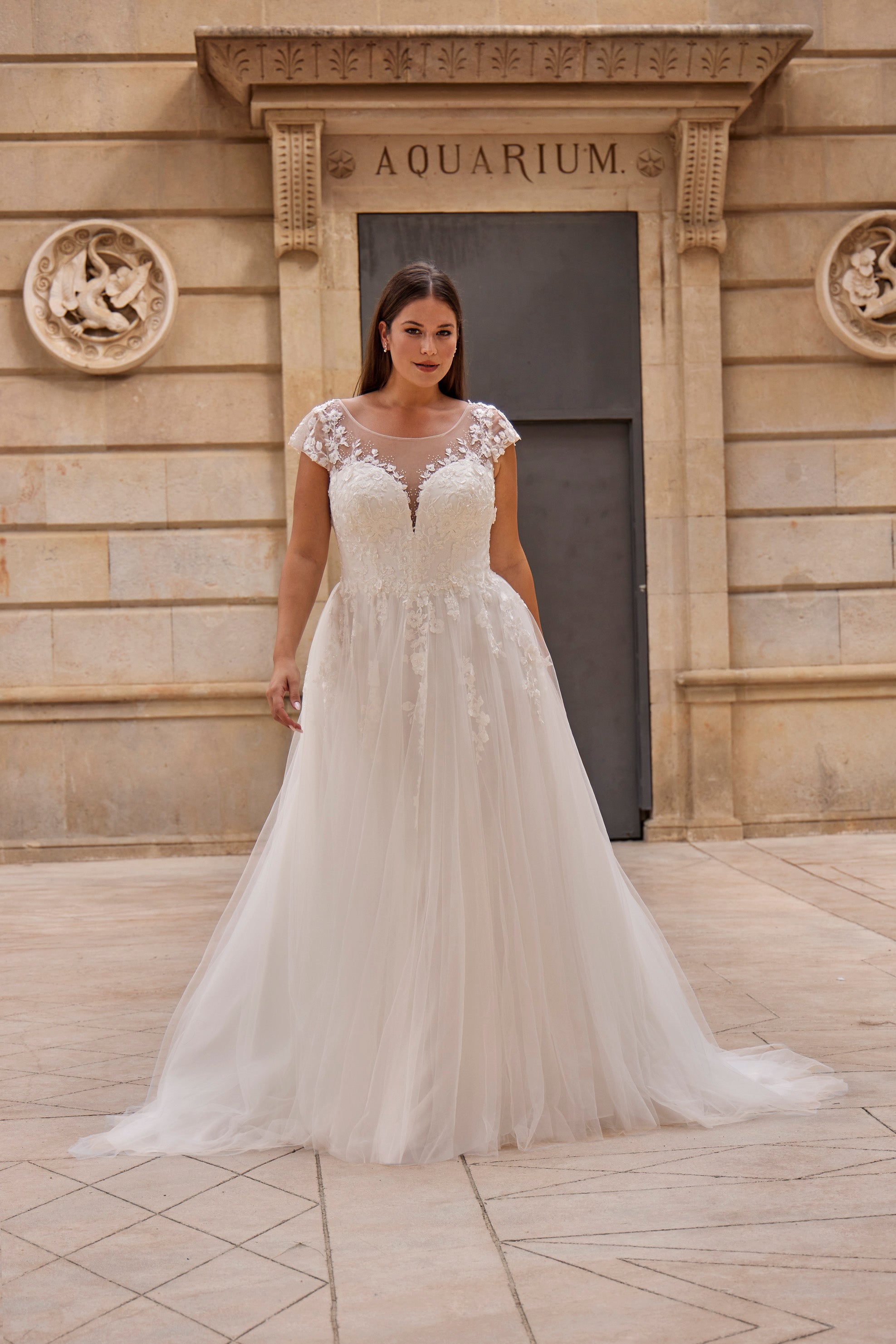 Woman in a white wedding dress standing in front of an 'Aquarium' building.