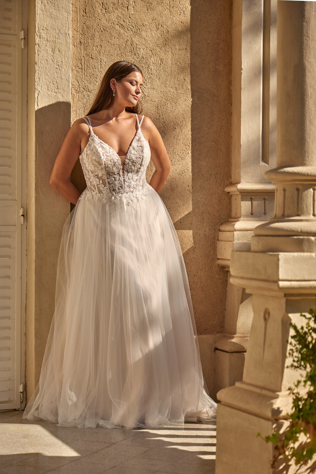 Woman in a white wedding dress standing outdoors against a stone wall.