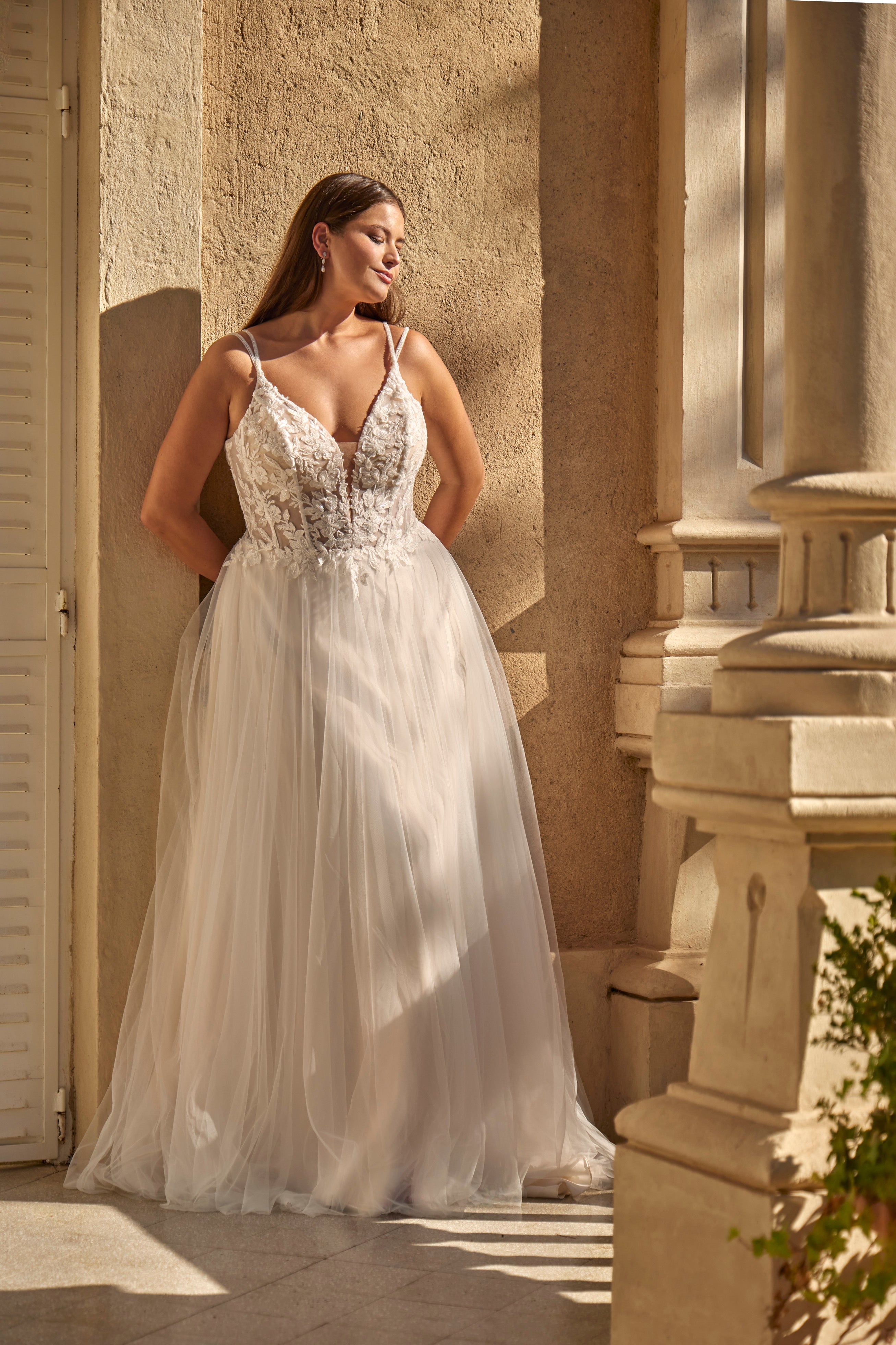 Woman in a white wedding dress standing outdoors against a stone wall.