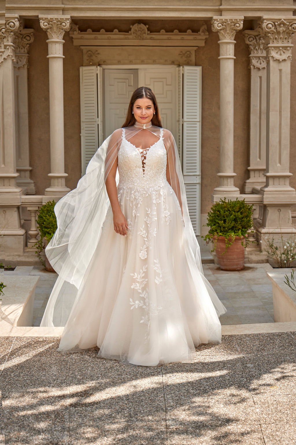 Woman in a white wedding dress with a long train standing in front of a classical building.