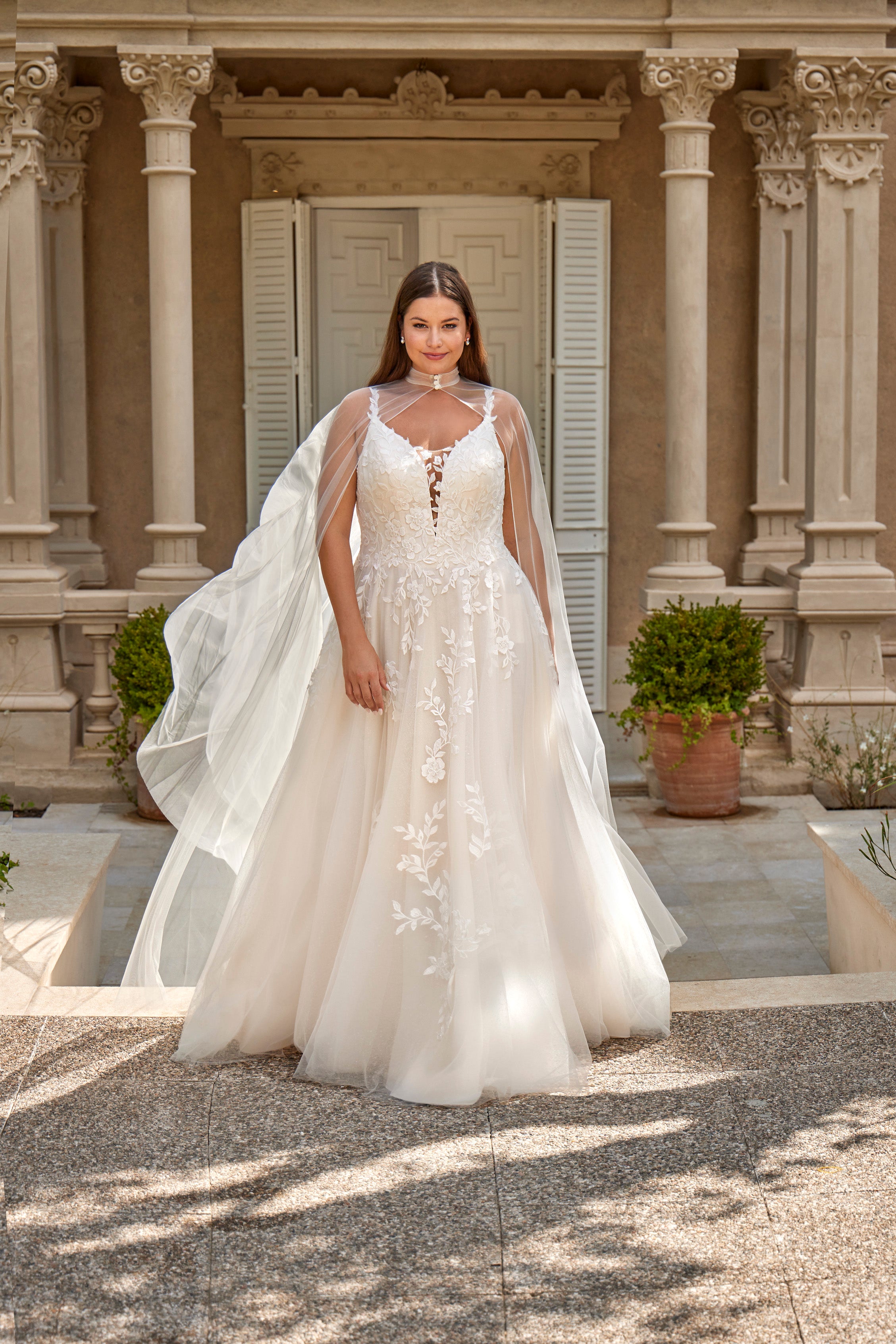 Woman in a white wedding dress with a long train standing in front of a classical building.
