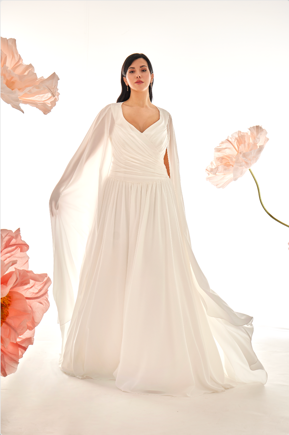 Woman wearing a white gown with a cape, surrounded by pink flowers on a light background