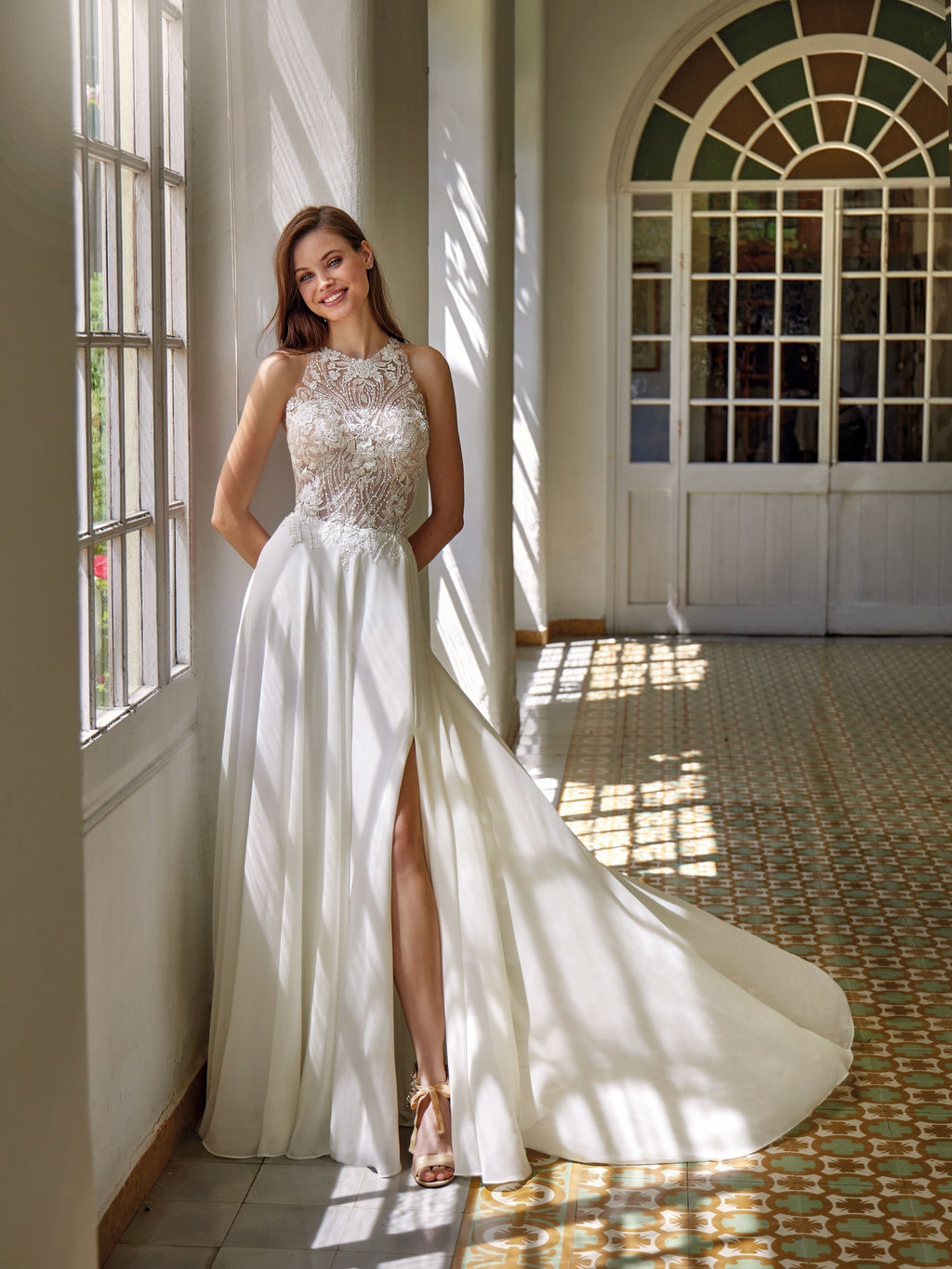 Woman in a white gown with a high slit standing in a sunlit room.