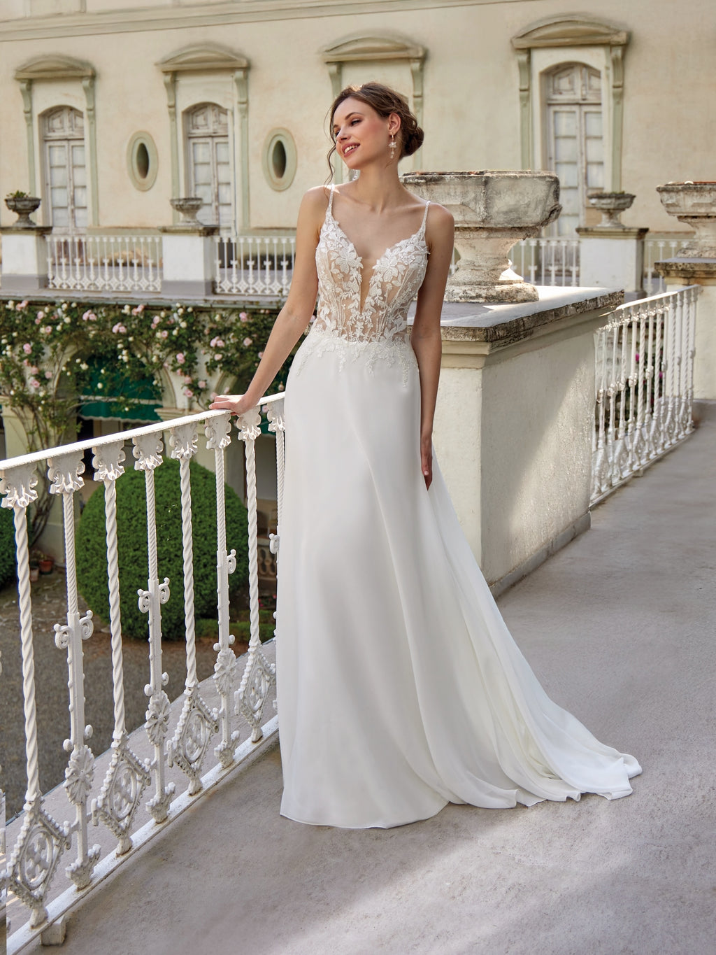 Woman in a white wedding dress standing on a balcony with classical architecture in the background