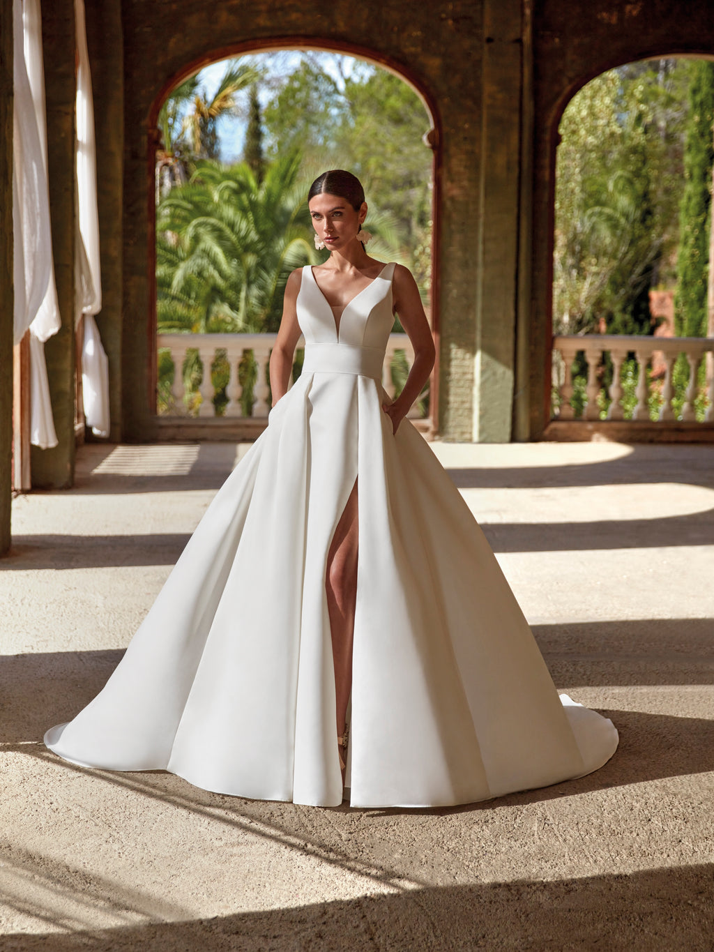 Woman in a white wedding dress standing in an outdoor setting with arches and greenery.