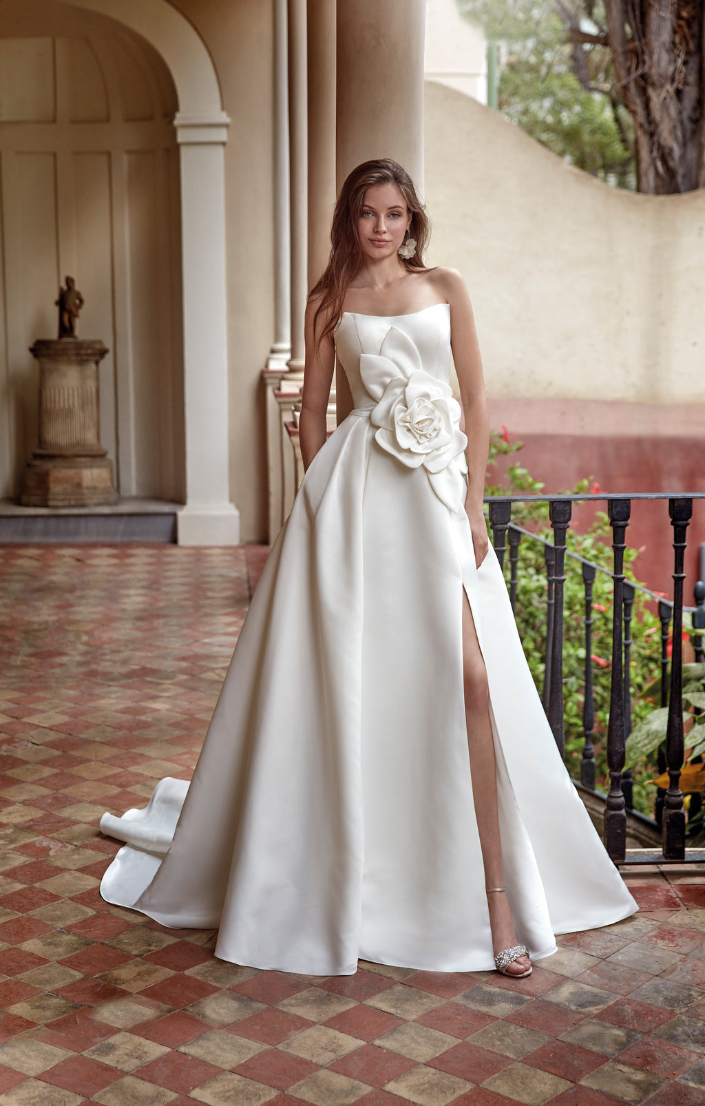 Woman in a white strapless gown with floral details standing on a patterned floor.