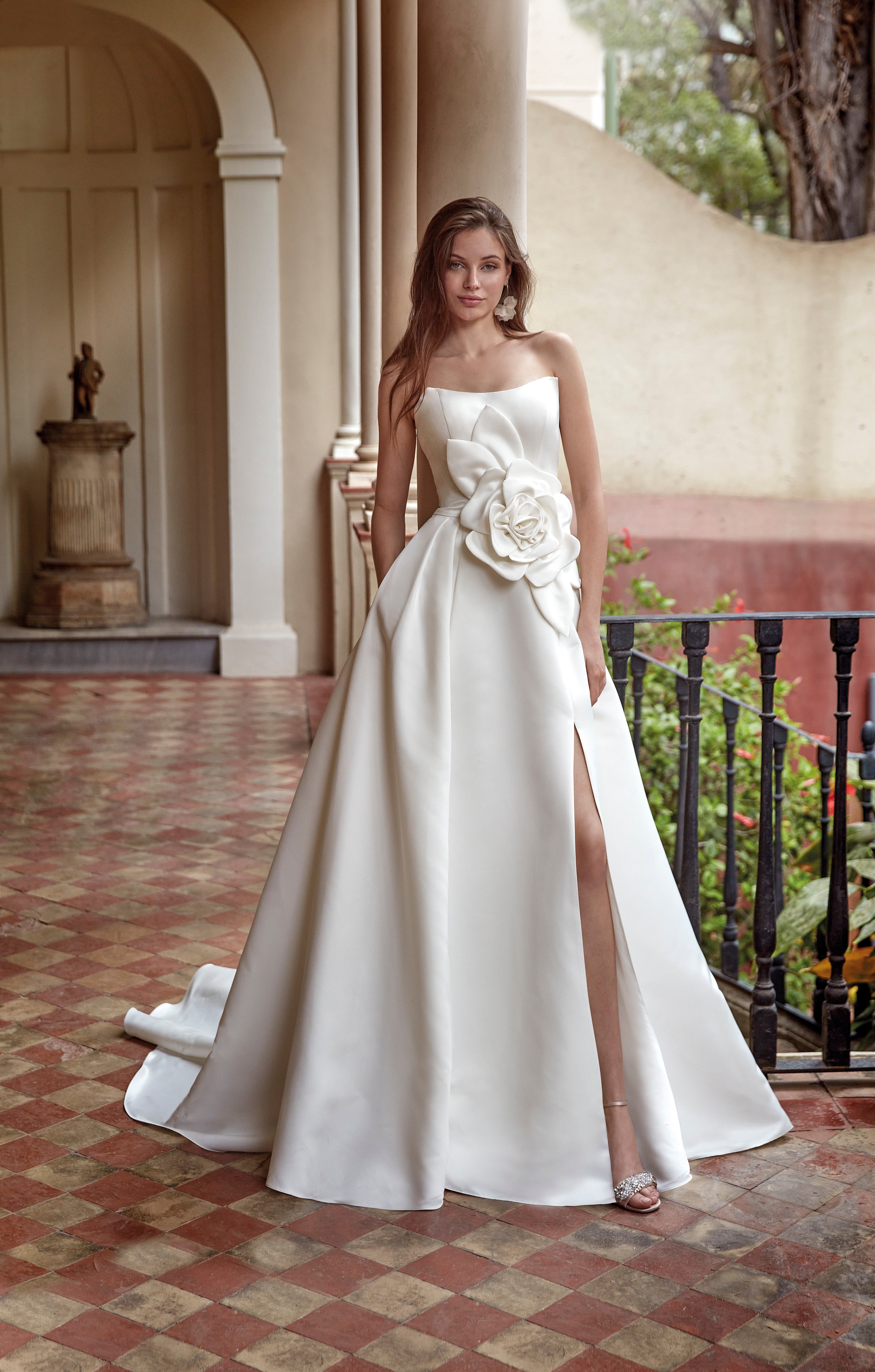 Woman in a white strapless gown with floral details standing on a patterned floor.