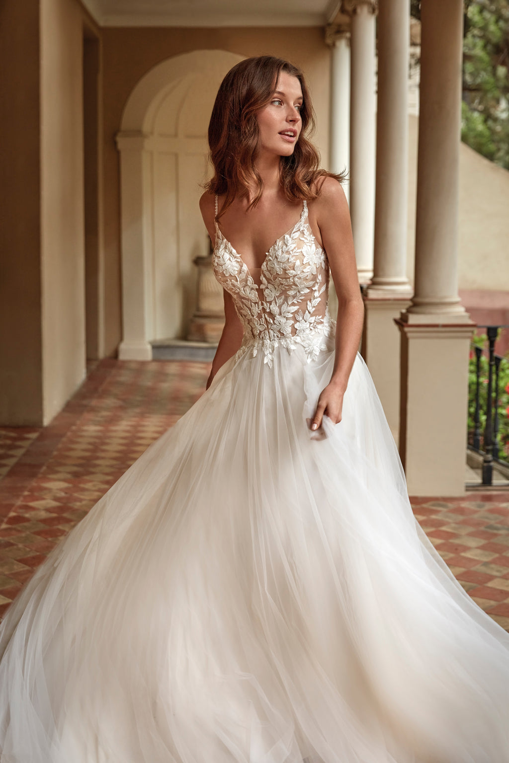 Woman in a white wedding dress with floral details standing in an elegant outdoor setting.