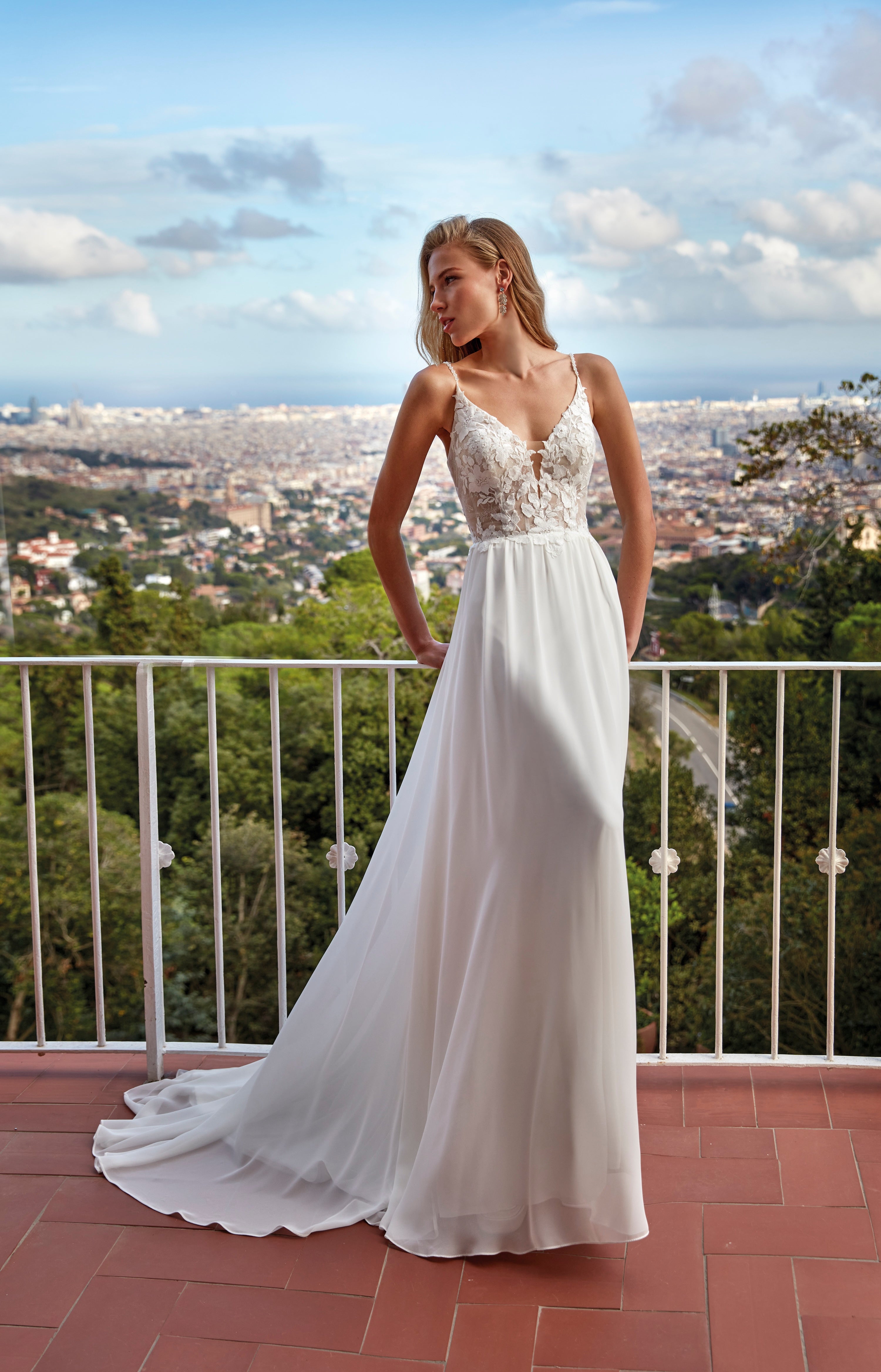 Woman in a white wedding dress standing on a balcony with a scenic view.