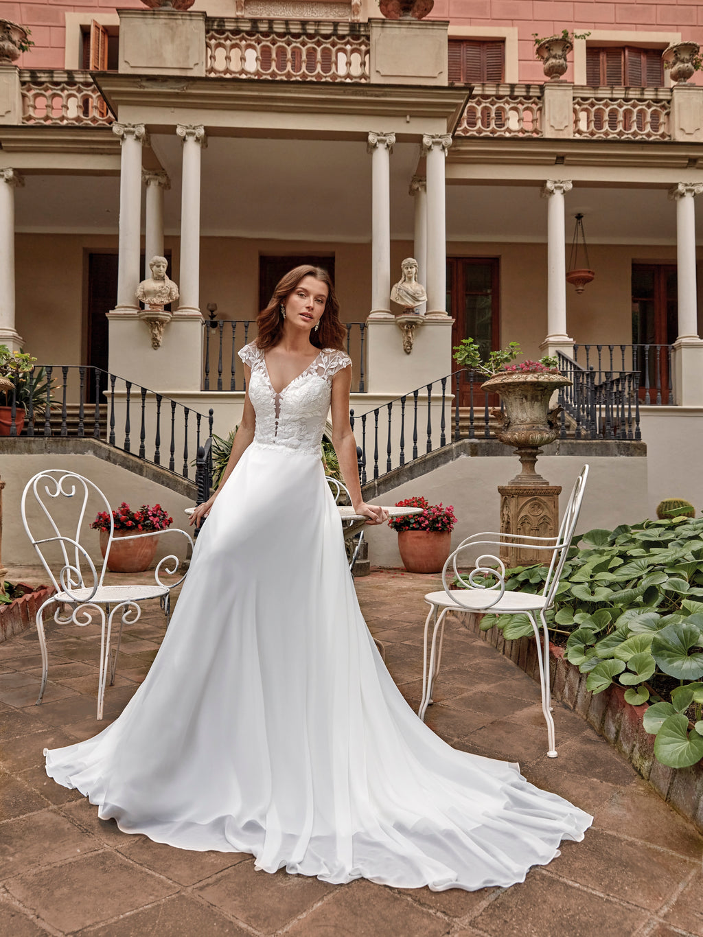 Woman in a white wedding dress standing in an elegant outdoor setting with columns and statues.