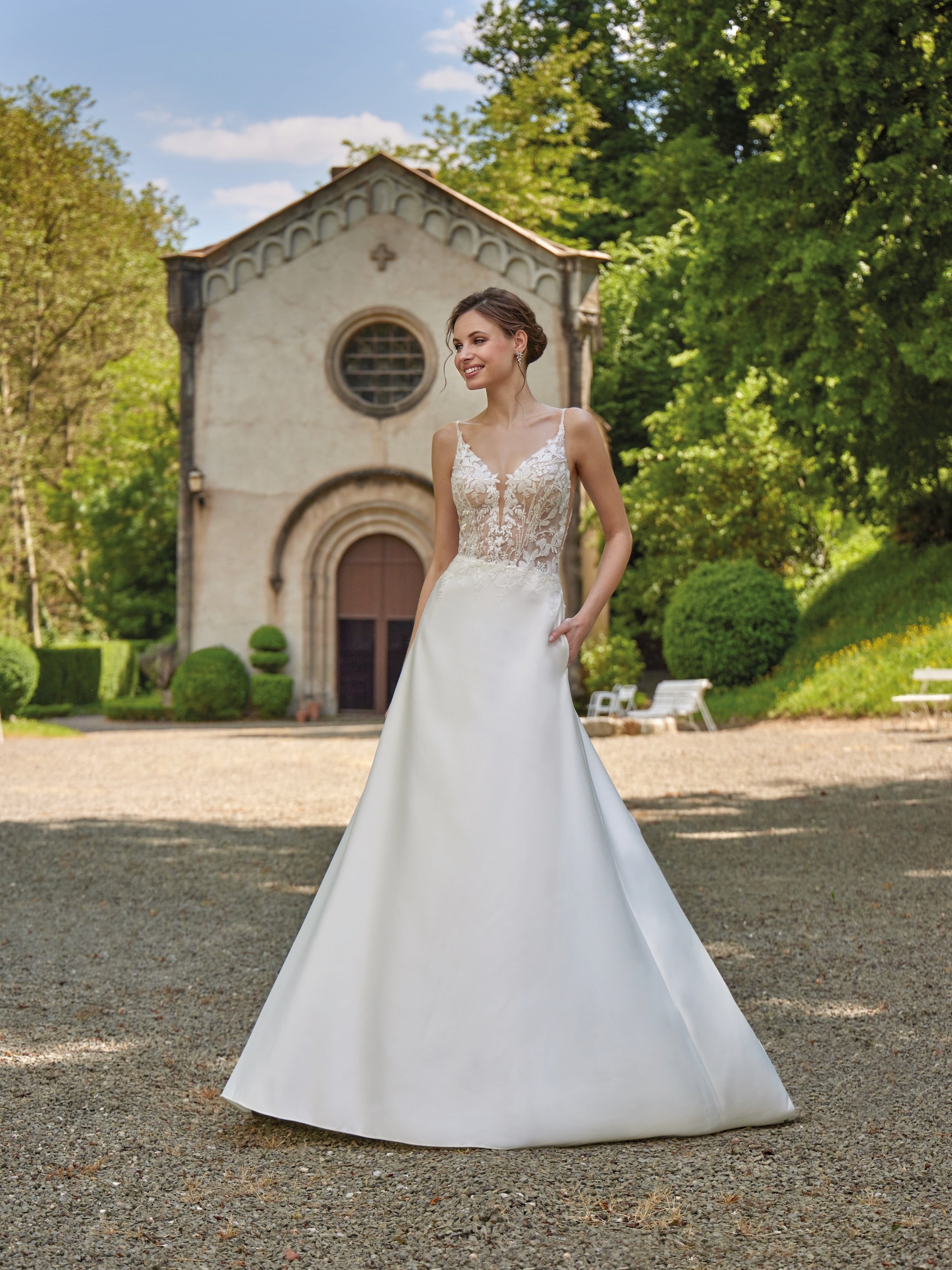 Woman in a white wedding dress standing in front of a small building with greenery.