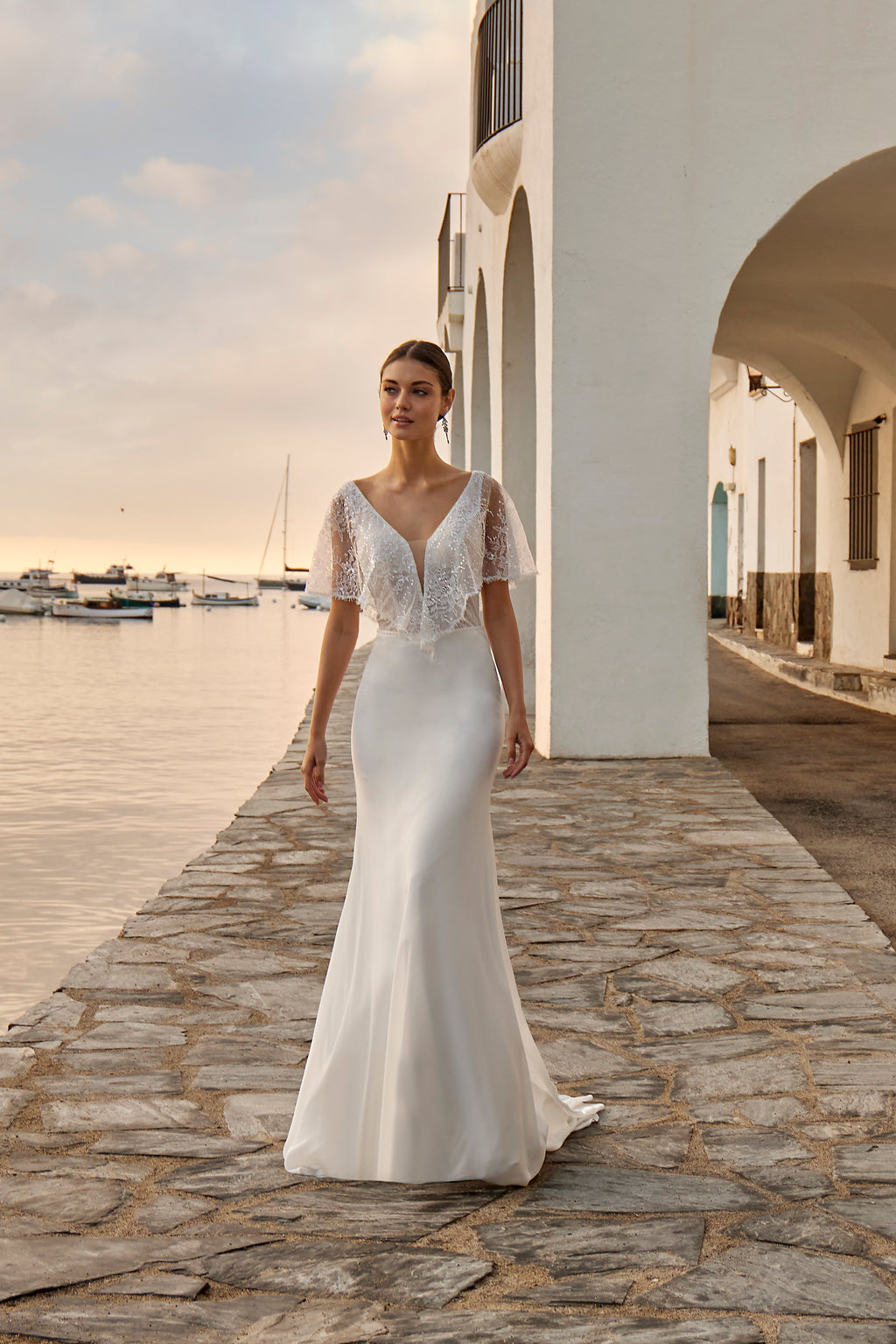 Woman in a white wedding dress standing on a stone pathway by a waterfront.