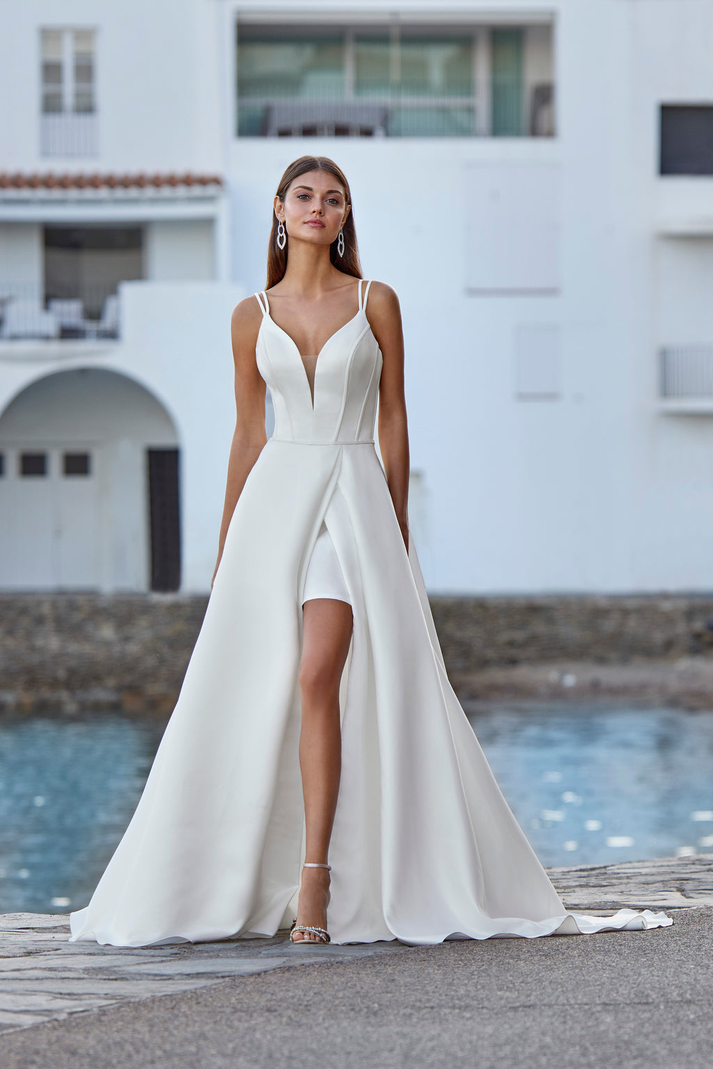 Woman in a white wedding dress standing by a pool with a building in the background