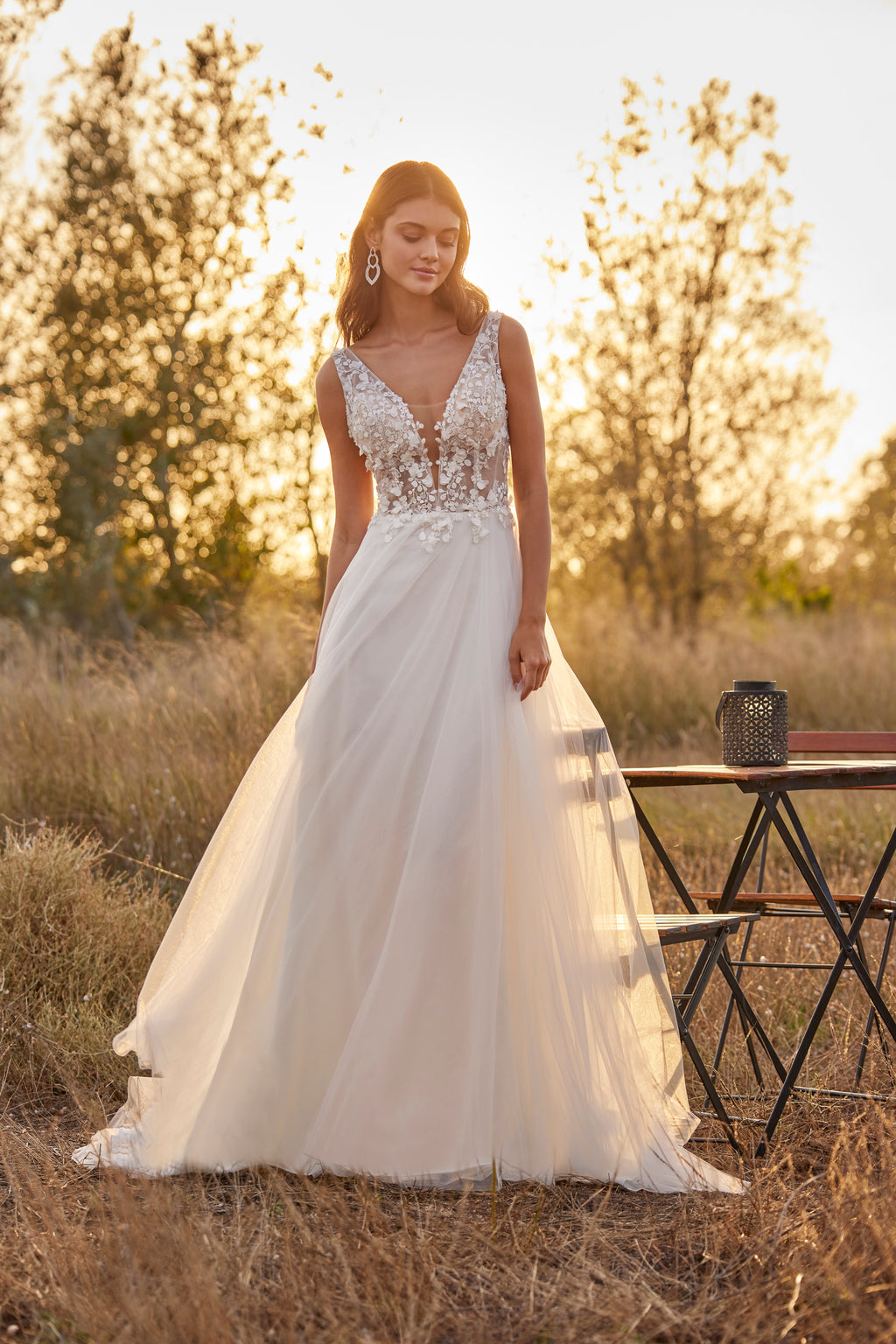 Woman in a white wedding dress standing in a field with a sunset background