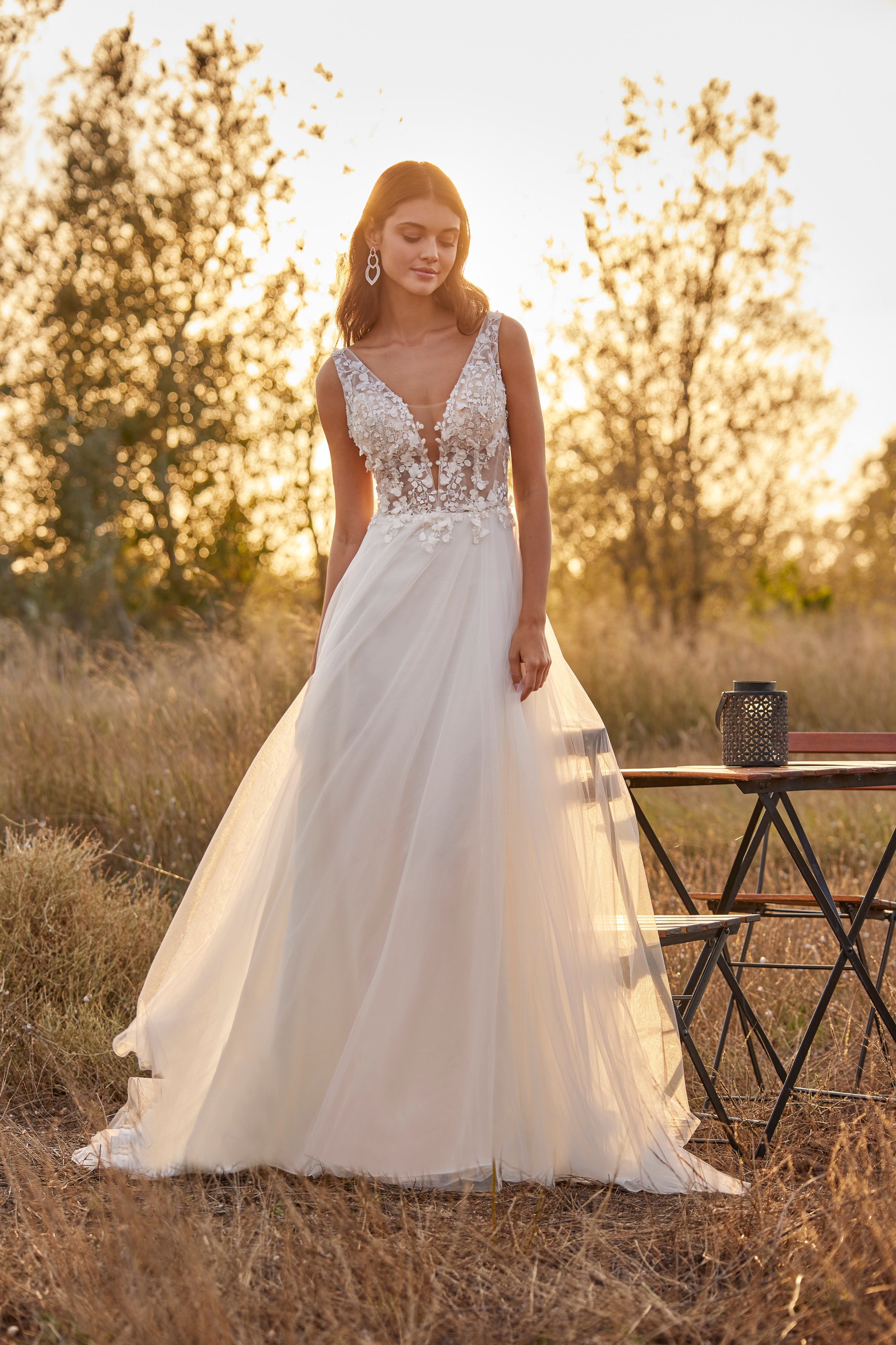 Woman in a white wedding dress standing in a field with a sunset background