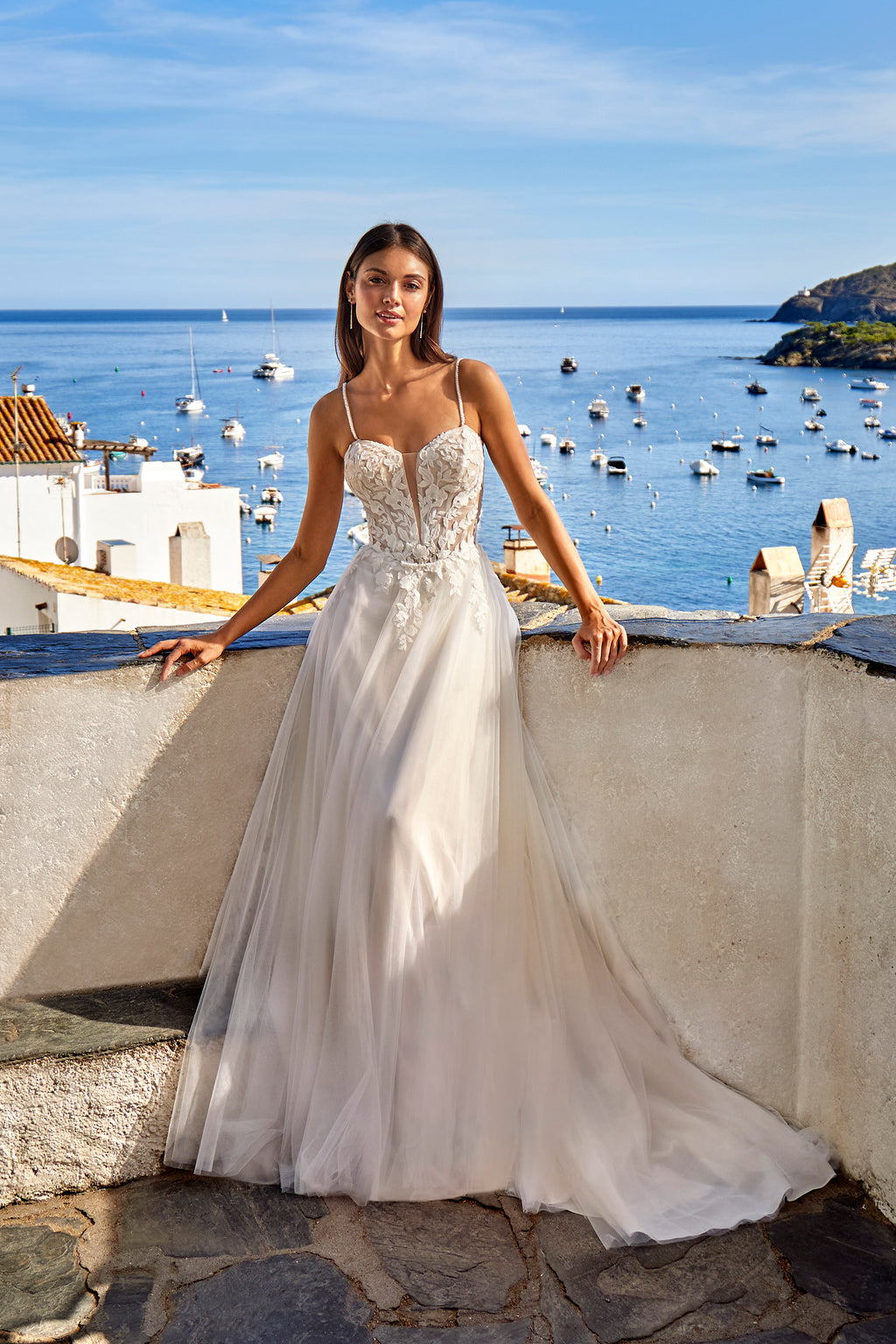 Woman in a white wedding dress standing on a balcony with a scenic ocean view.
