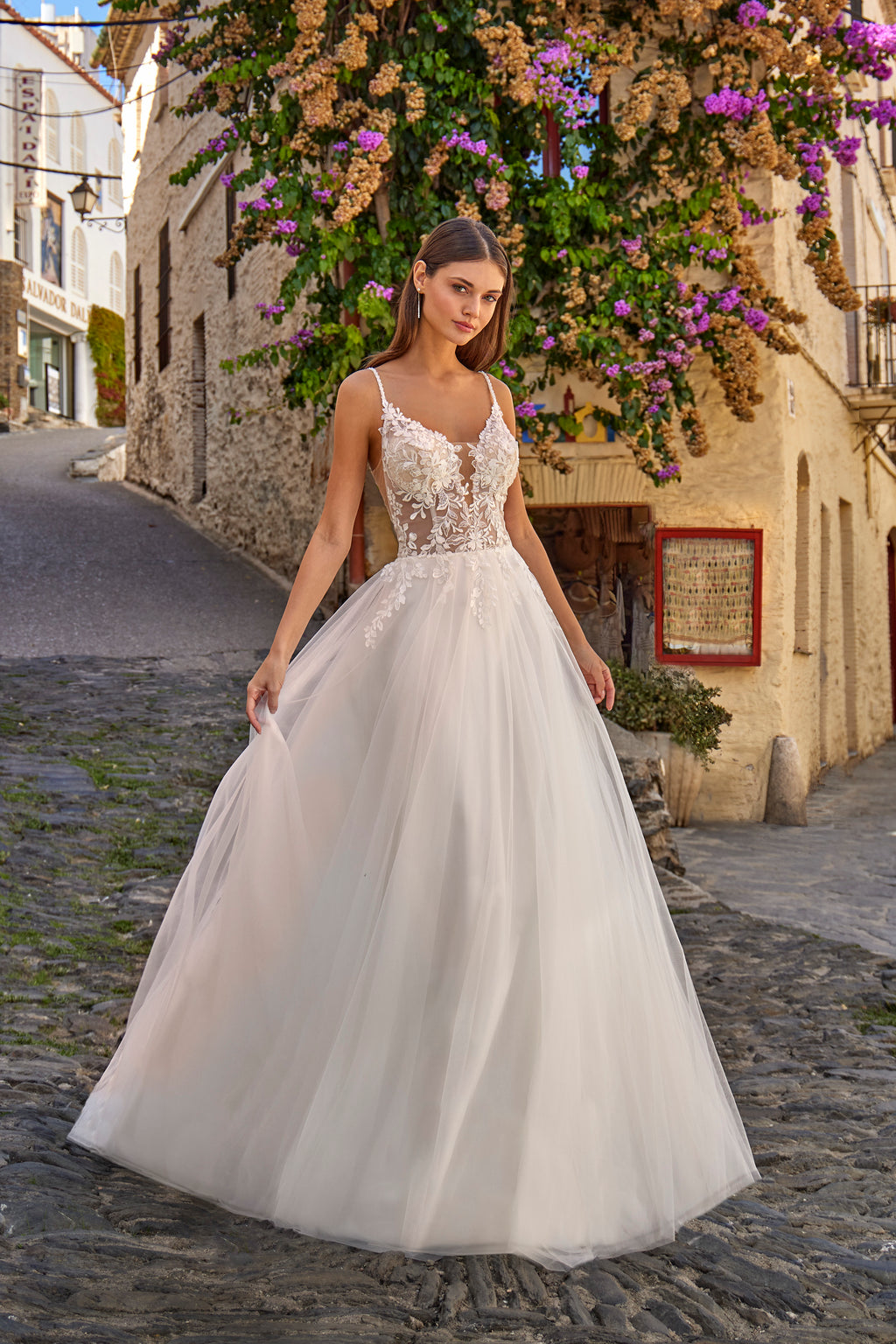 Woman in a white wedding dress standing on a cobblestone street with floral decorations.
