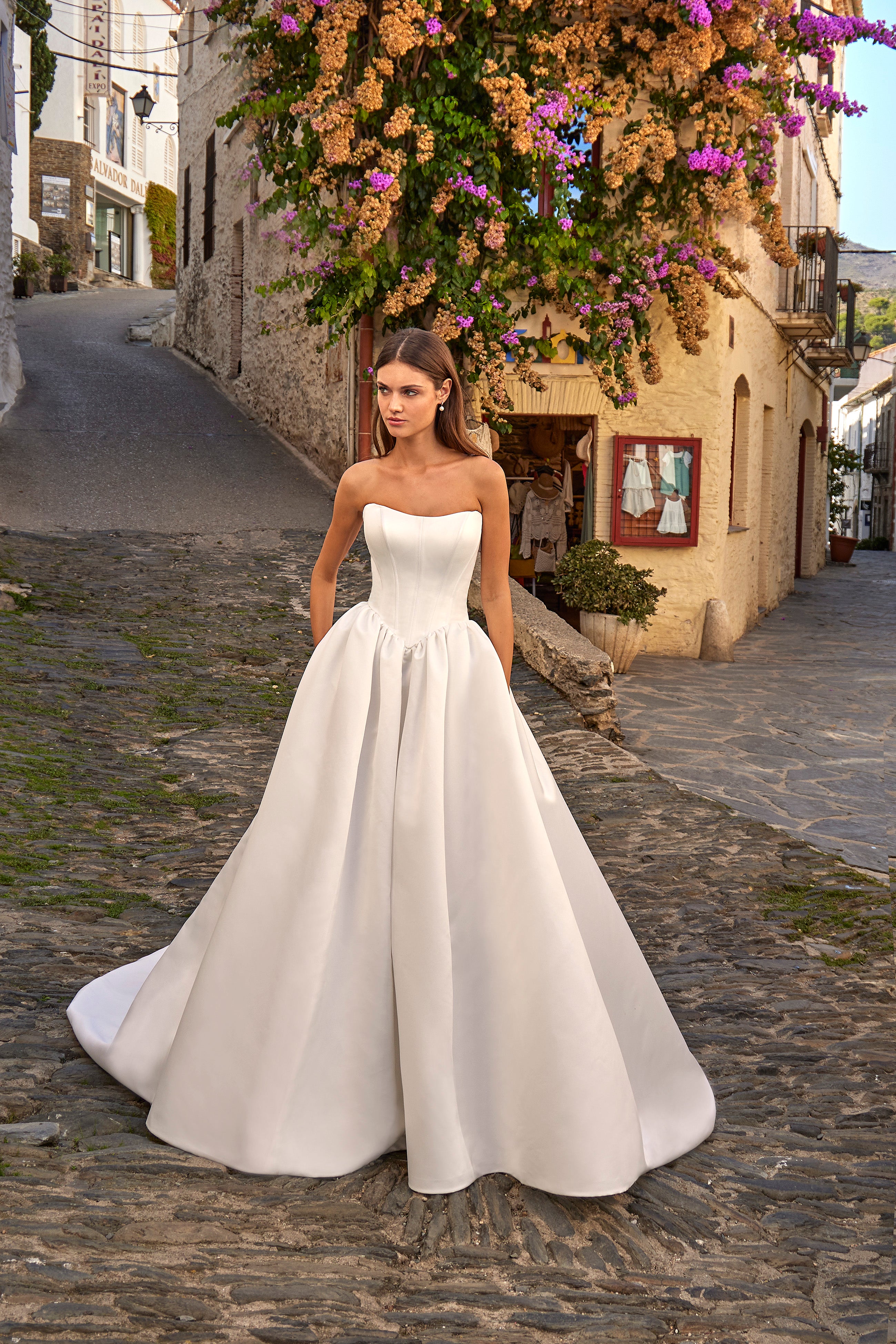 Woman in a white strapless gown standing on a stone street with floral decorations.