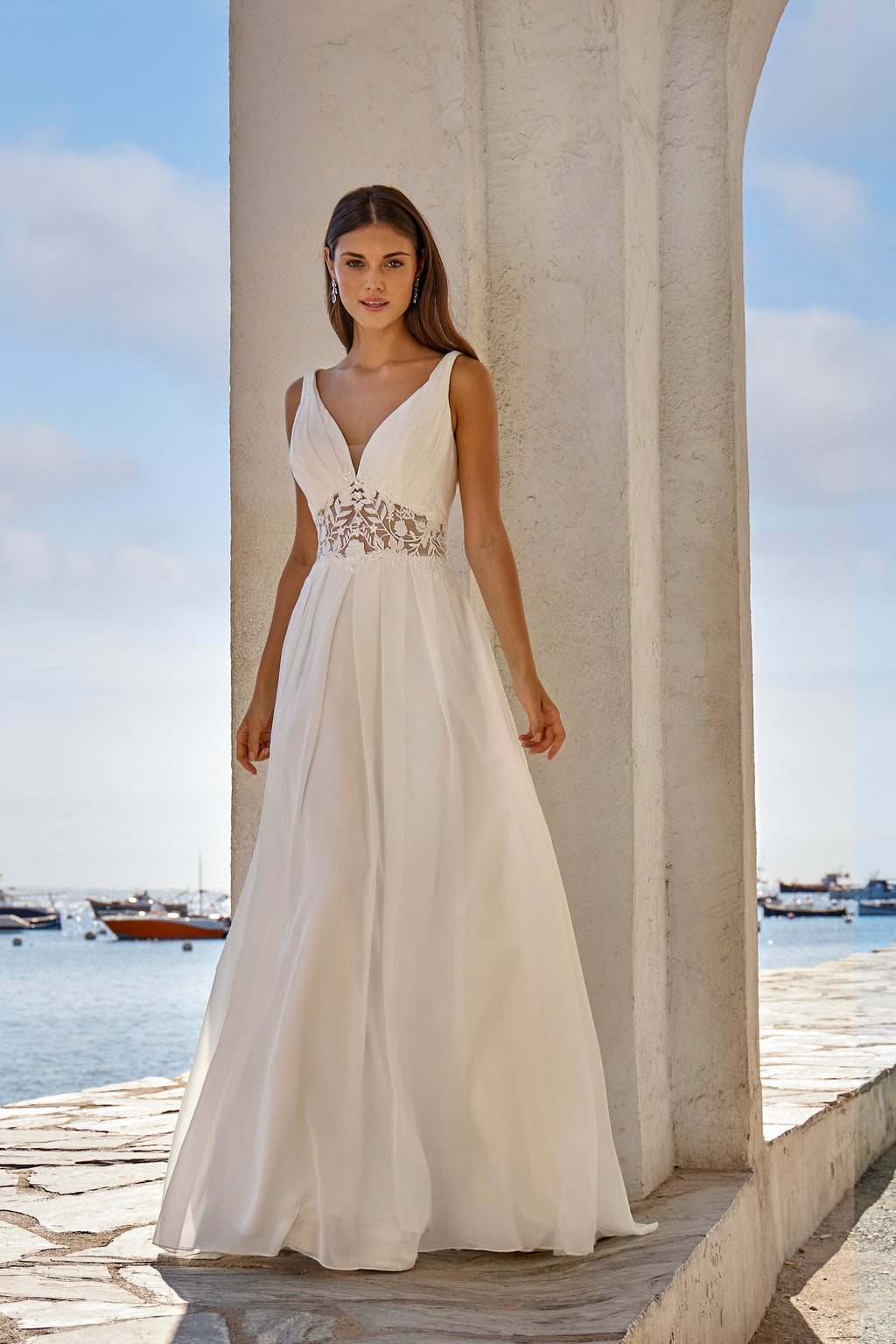 Woman in a white wedding dress standing by a waterfront with boats in the background