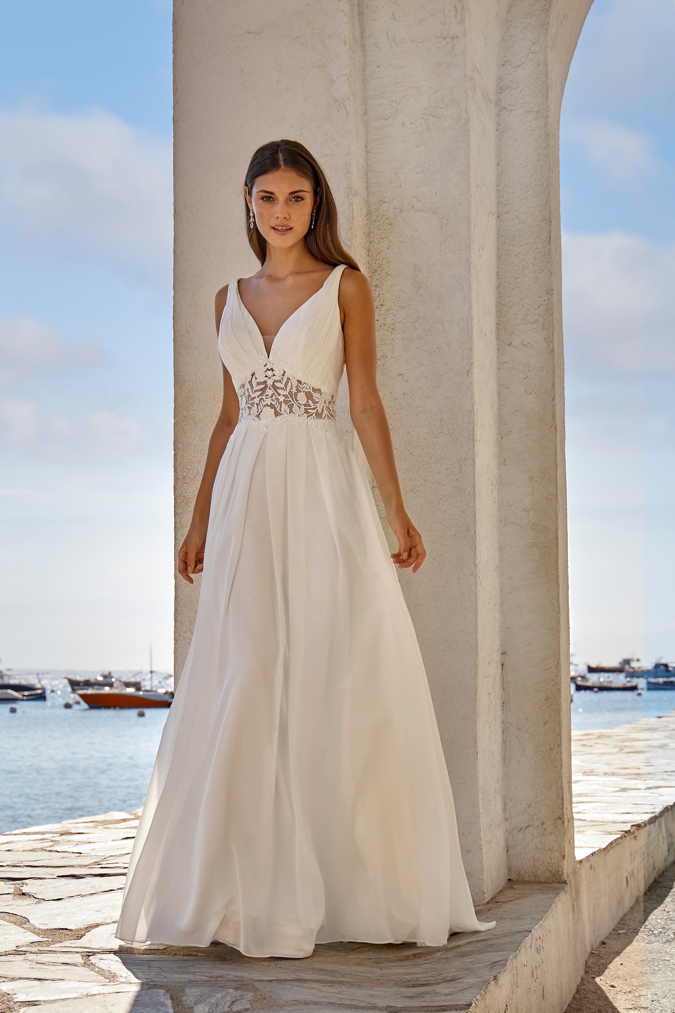 Woman in a white wedding dress standing by a waterfront with boats in the background