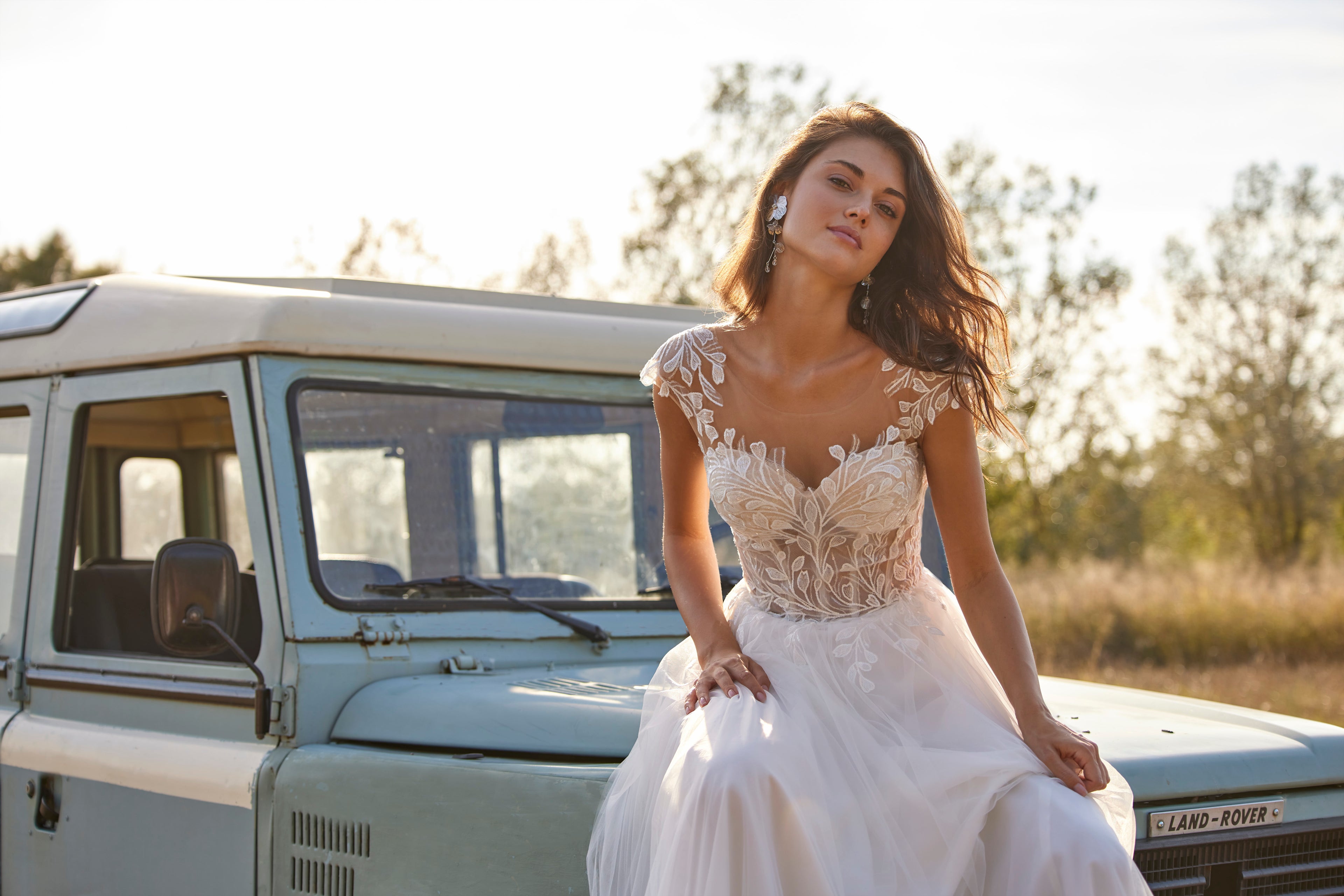 Woman in a wedding dress sitting on an old-fashioned vehicle in a natural setting