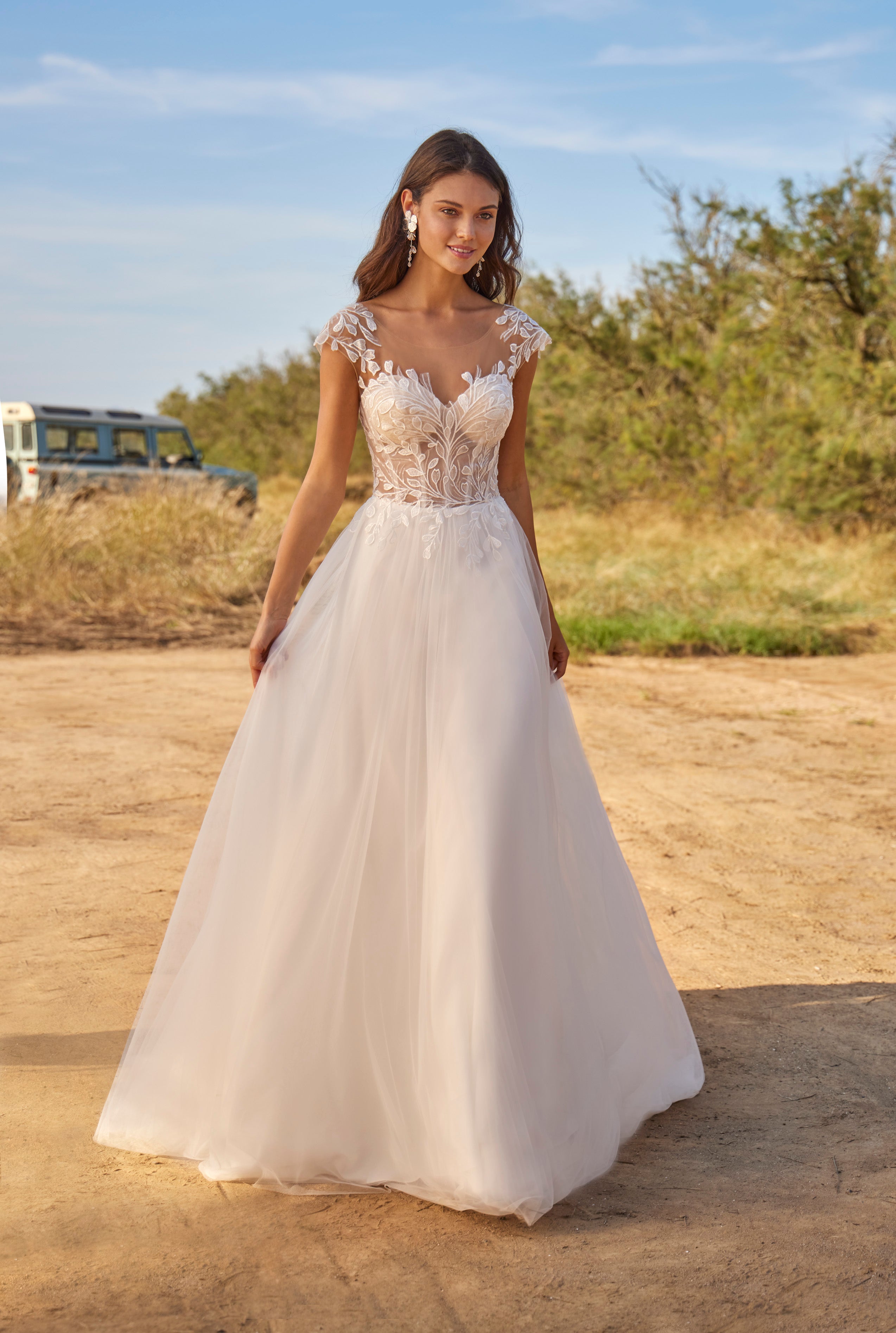 Woman in a white wedding dress standing in an outdoor setting with trees and a clear sky.