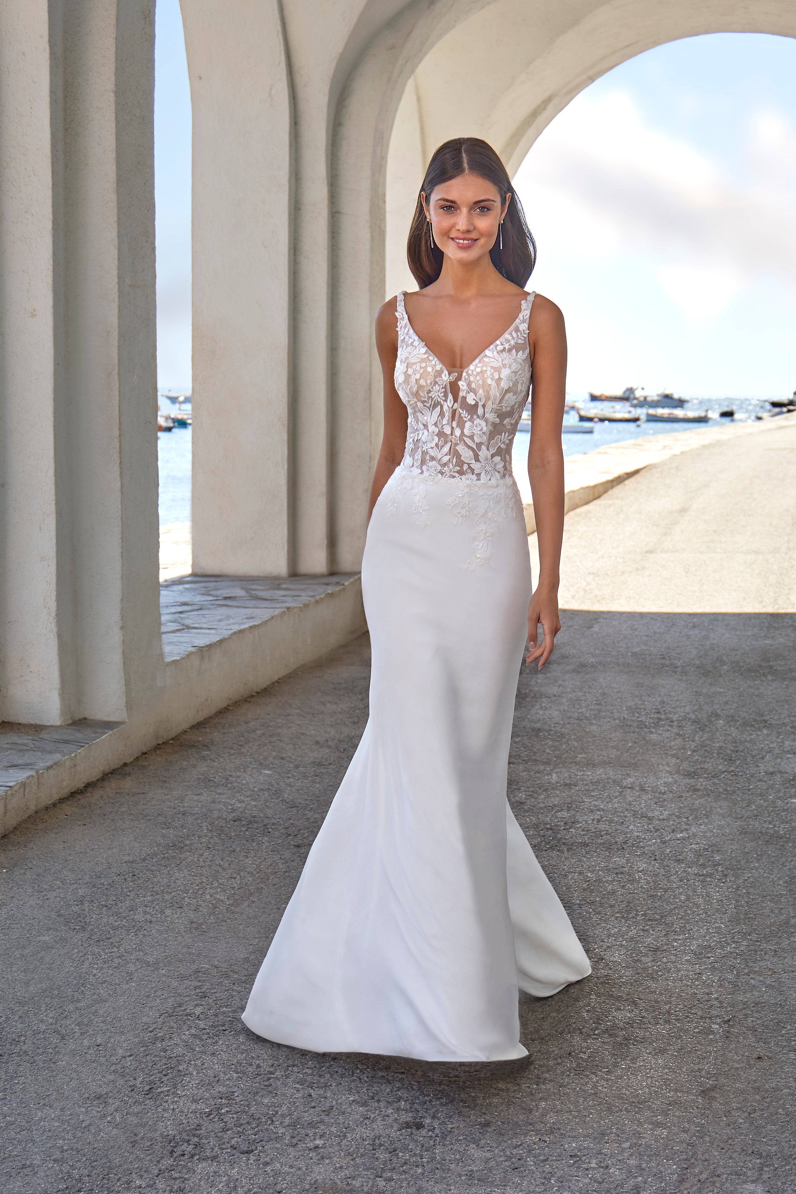 Woman in a white wedding dress with floral lace details standing in front of a classical architecture building.