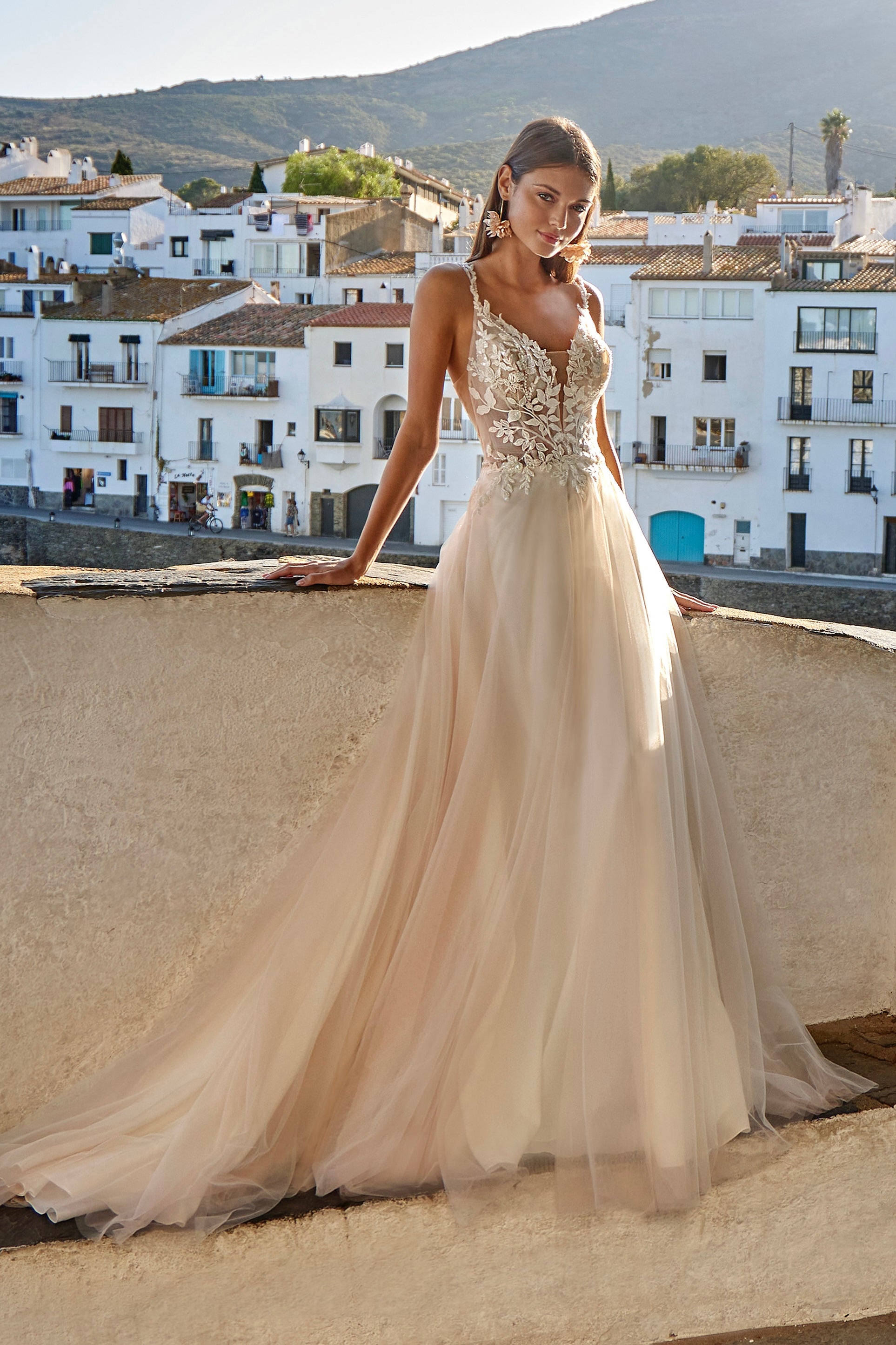 Woman in a beige wedding dress standing on a rooftop with a scenic town view.