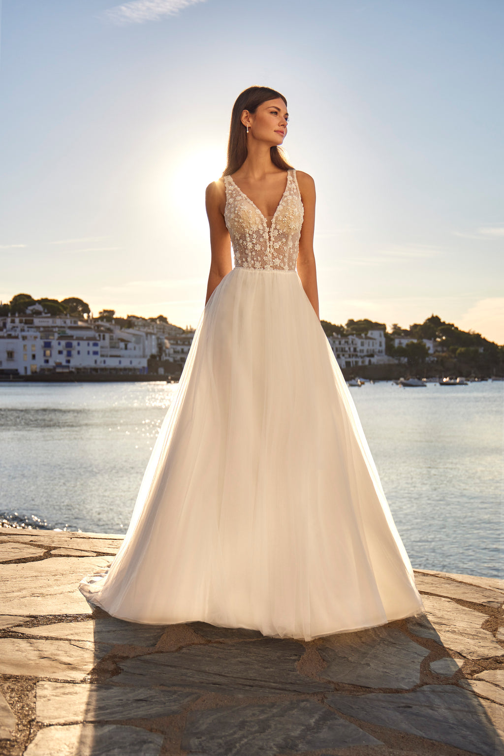 Woman in a white wedding dress with a scenic background of water and buildings.