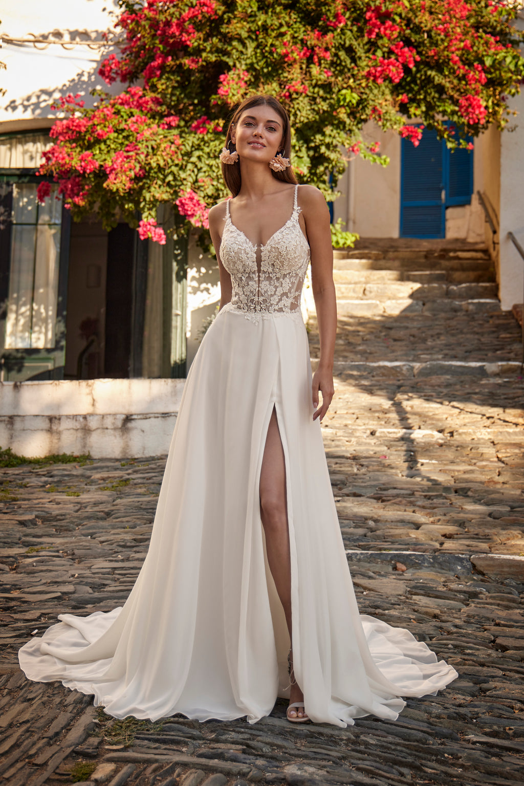 Woman in a white wedding dress with floral details standing on a stone path.