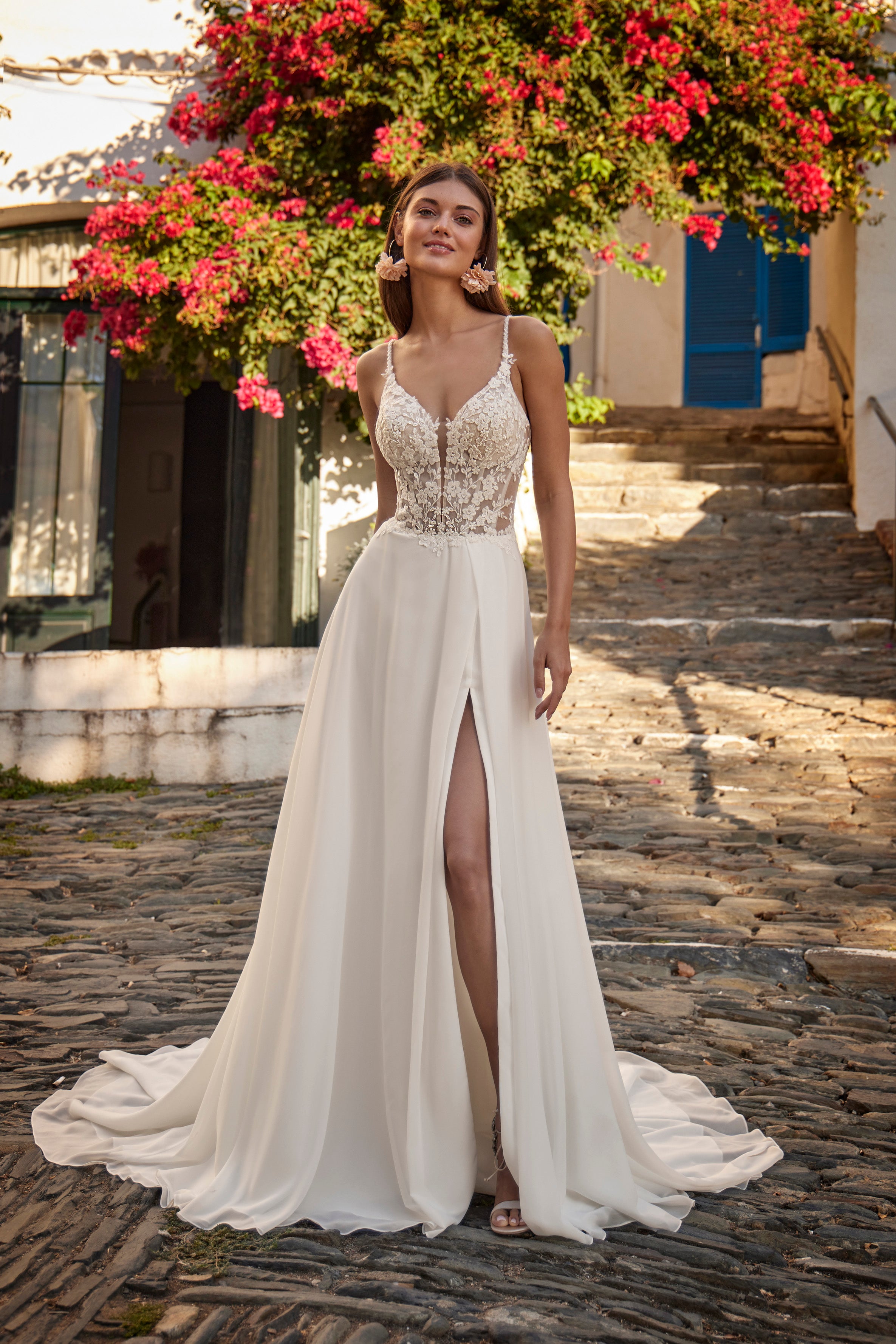 Woman in a white wedding dress with floral details standing on a stone path.