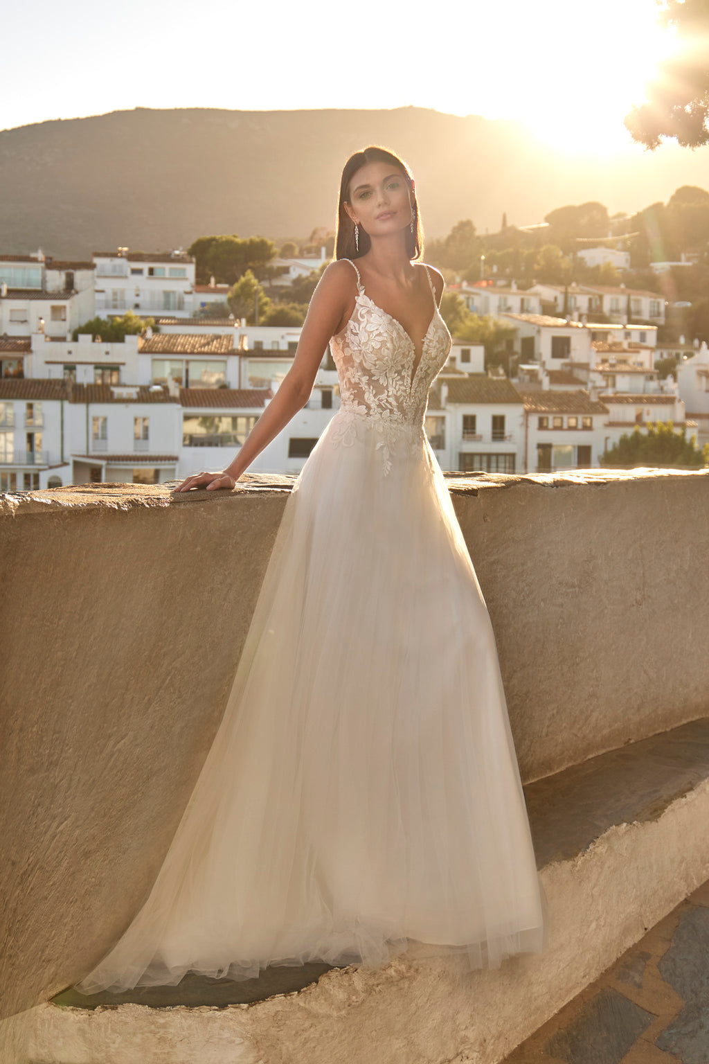 Woman in a white wedding dress standing on a balcony with a scenic town view.